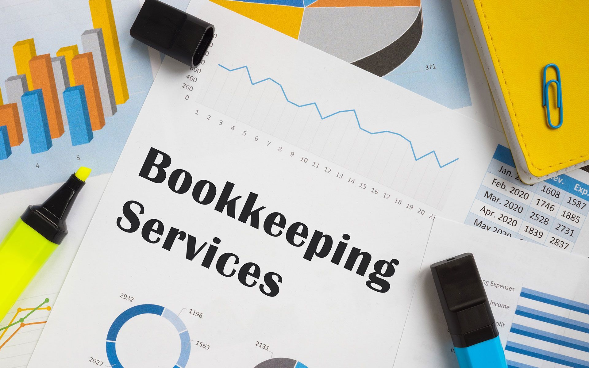 Bookkeeping Services document with charts, markers, and notebook on a desk.