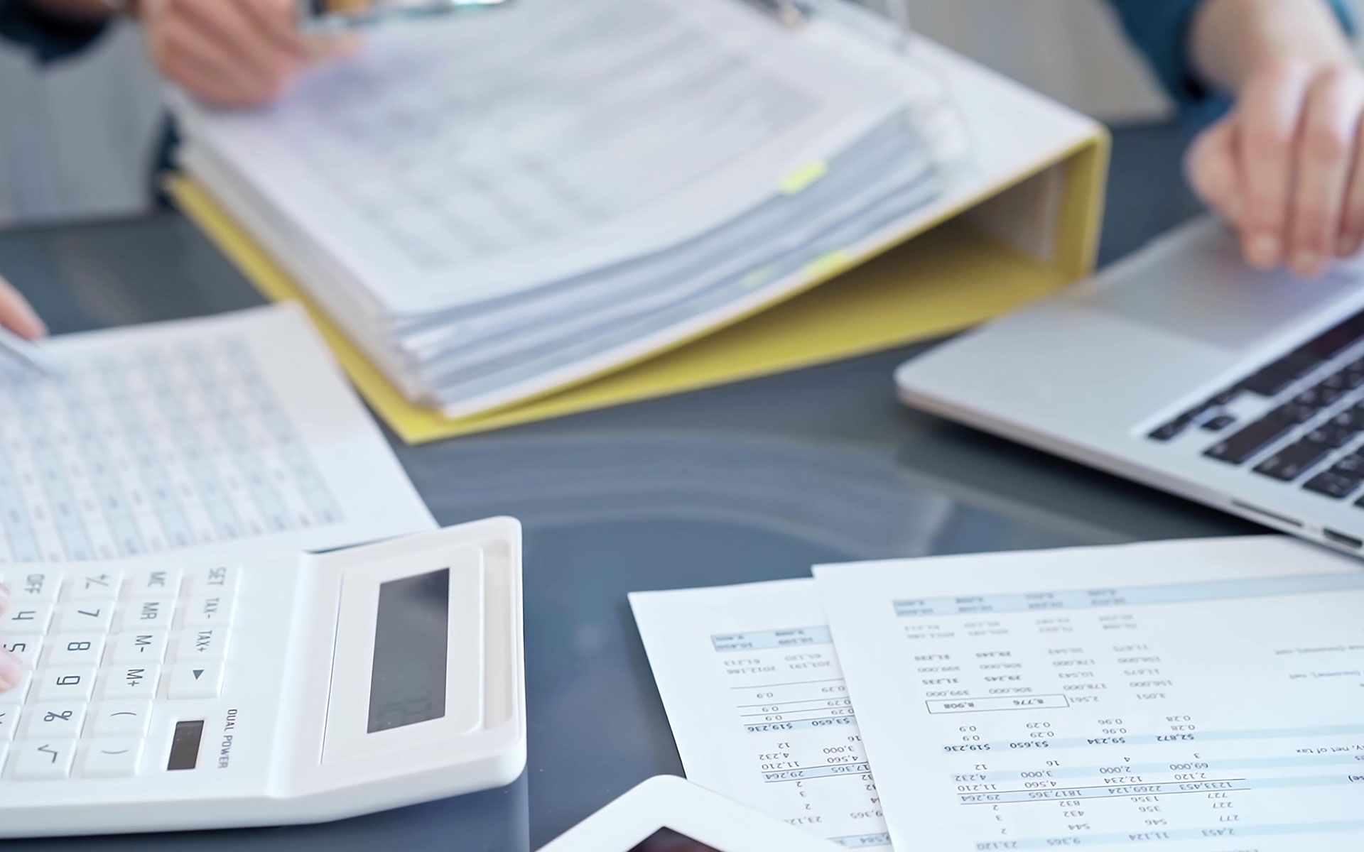 Person using calculator, laptop, and papers with financial documents.