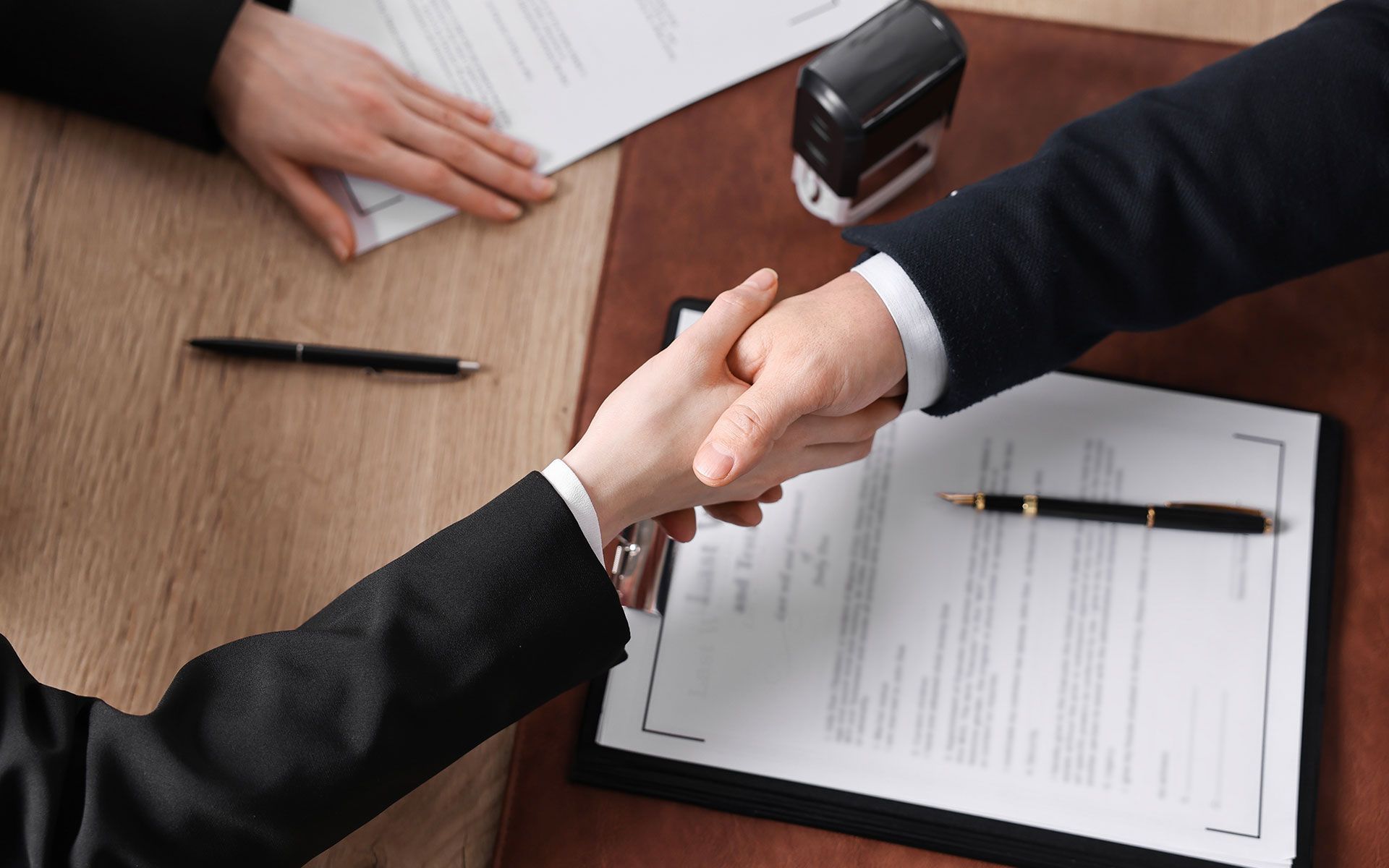 Two people in suits shaking hands over a contract.