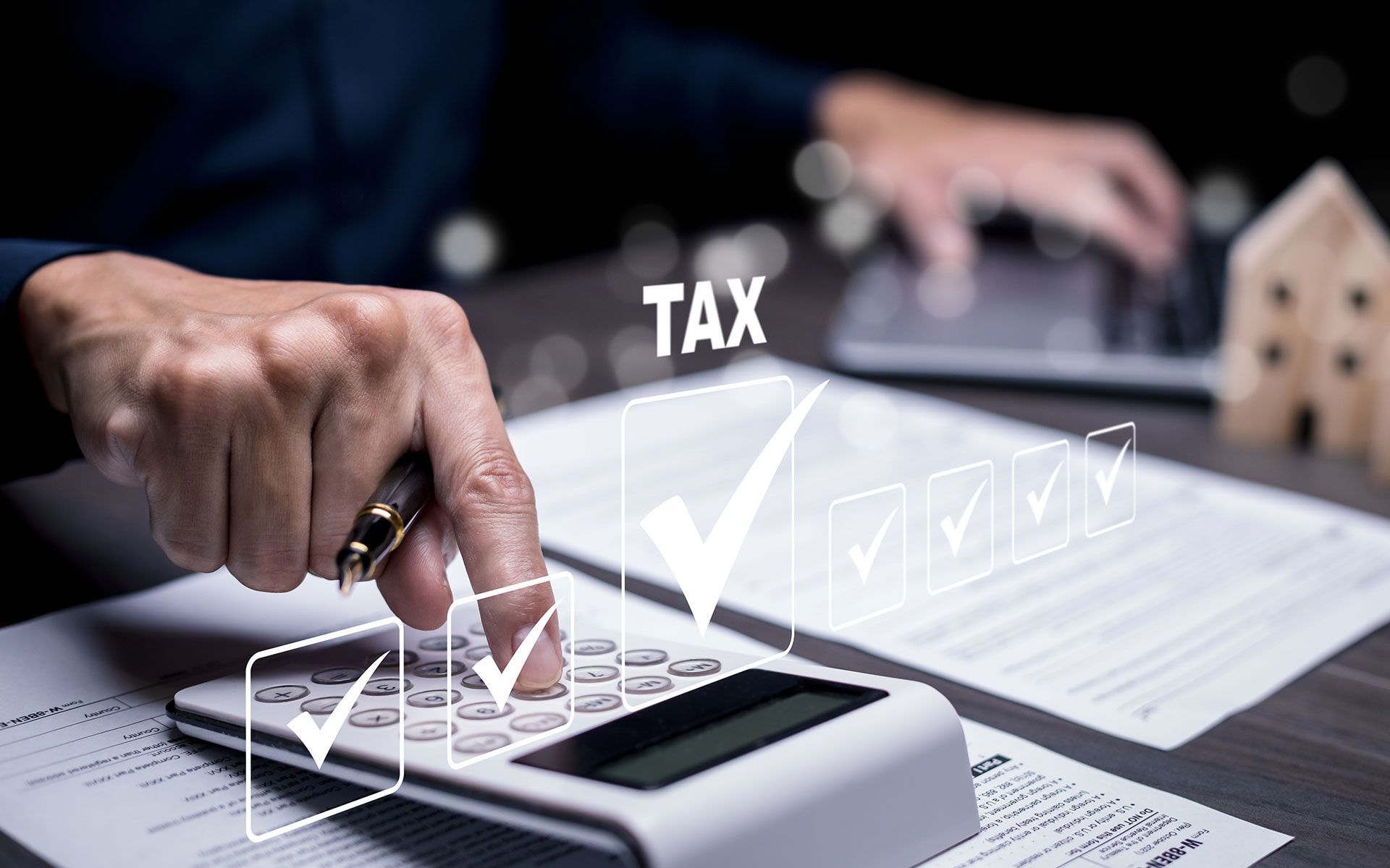 Person calculating taxes with a calculator, documents, and a house model.