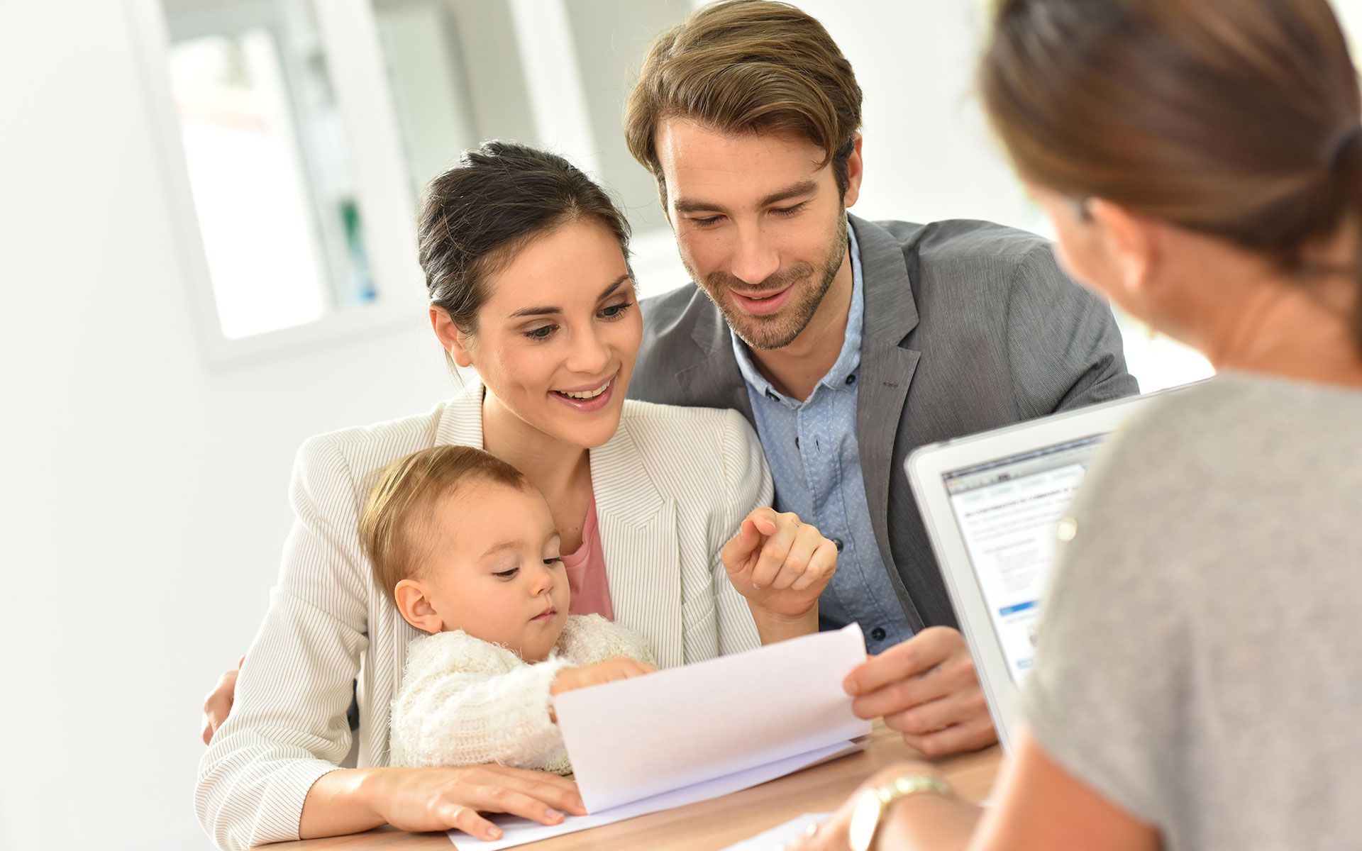 Family with baby reviewing documents with a person using a laptop at a table.