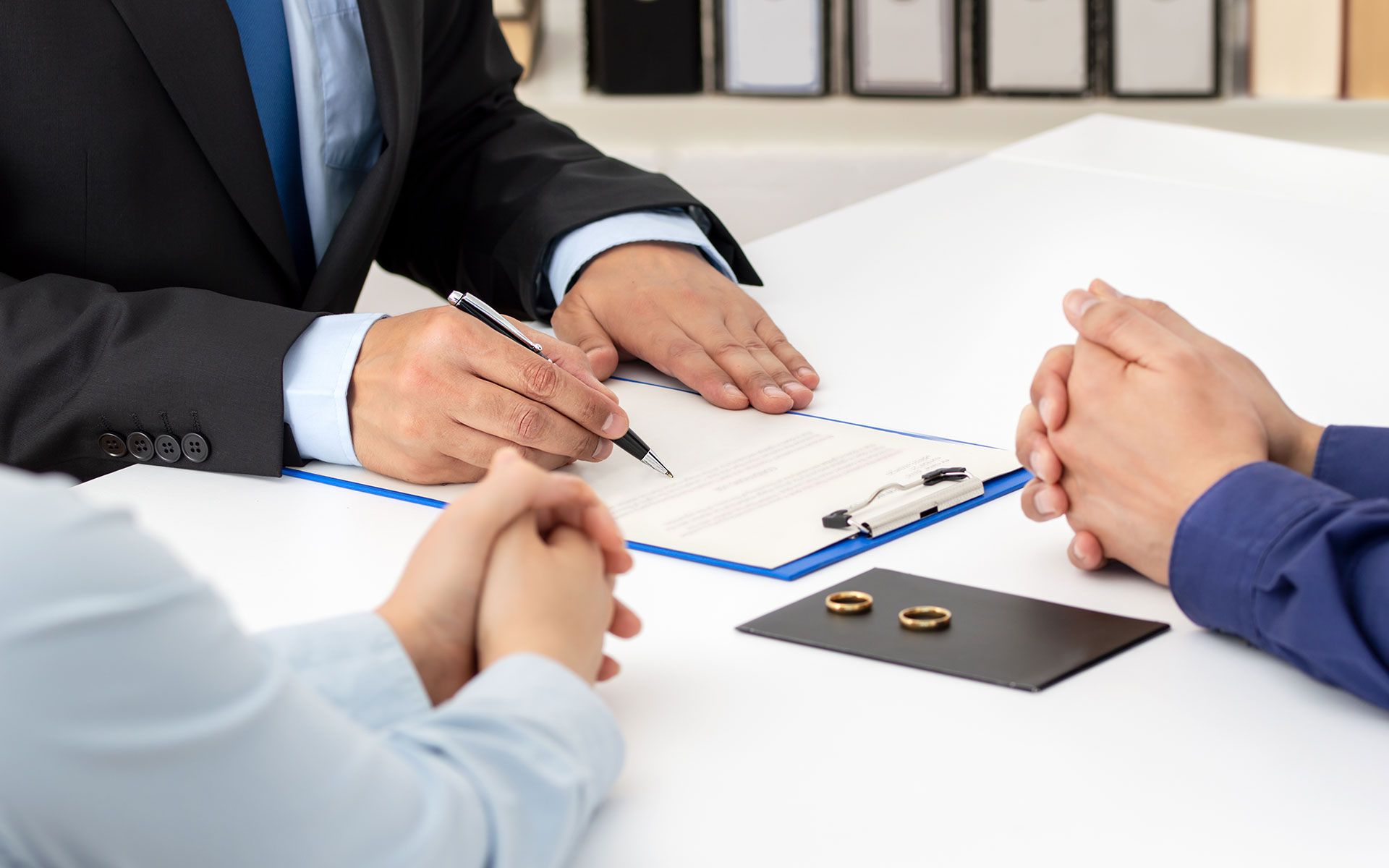 Lawyer signing divorce papers with couple; wedding rings on table.