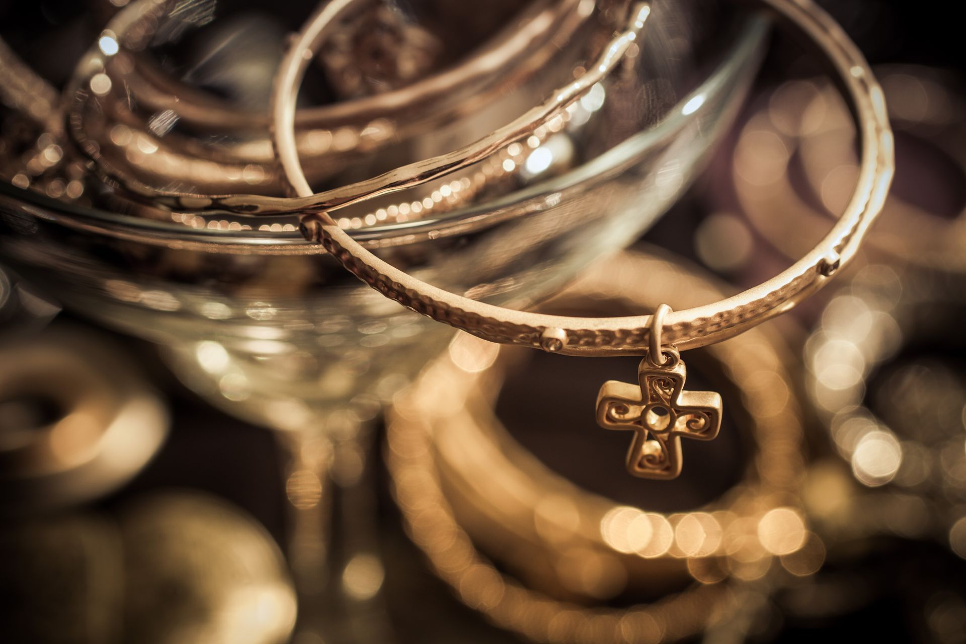 Stack of gold bangles with a cross pendant in a glass bowl