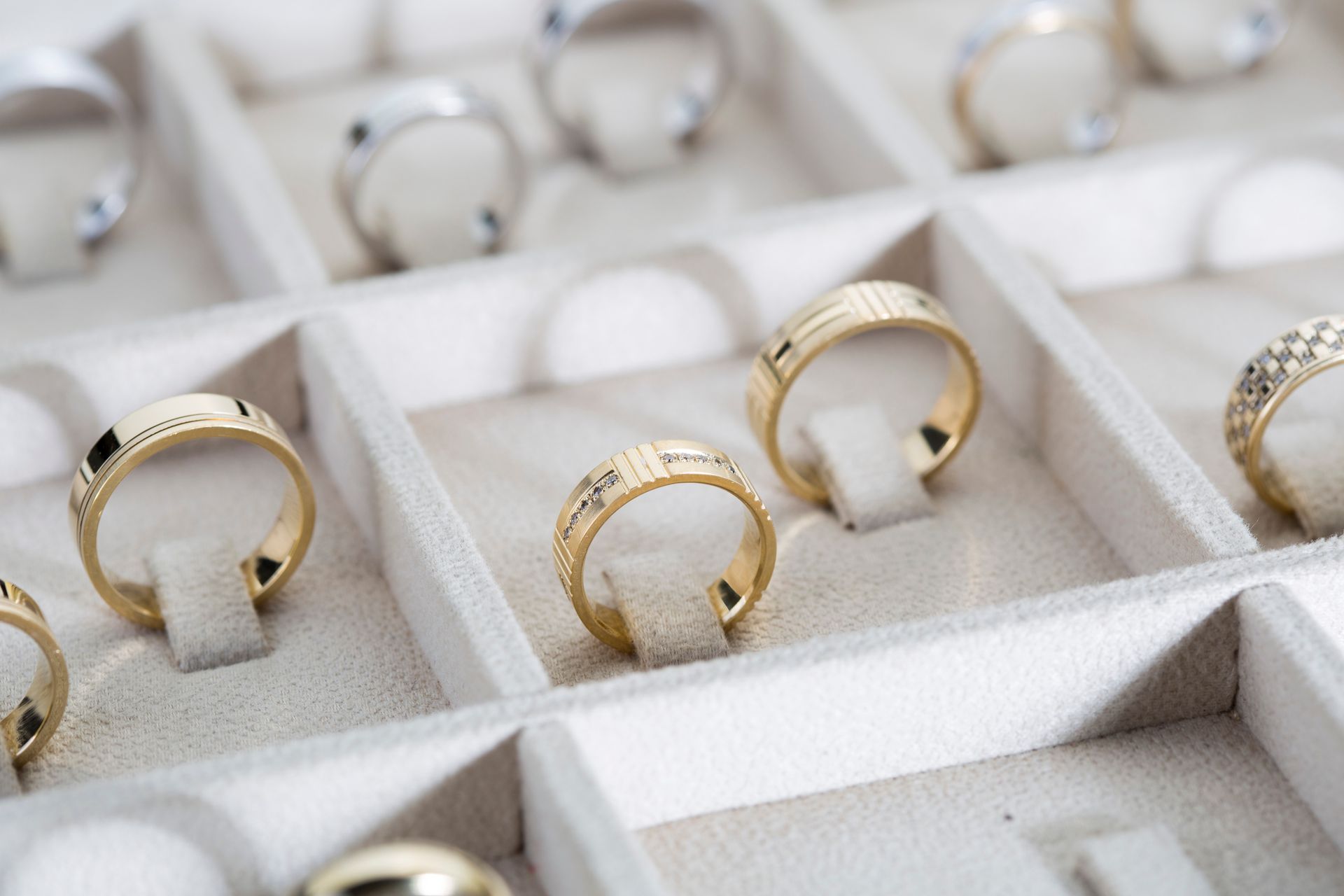 Multiple gold and diamond rings neatly organized in a soft white jewelry display tray.