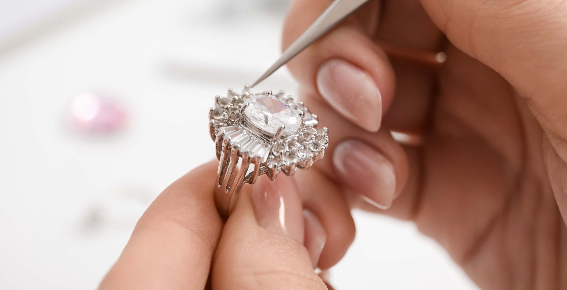 Hand holding a diamond ring with tweezers for inspection