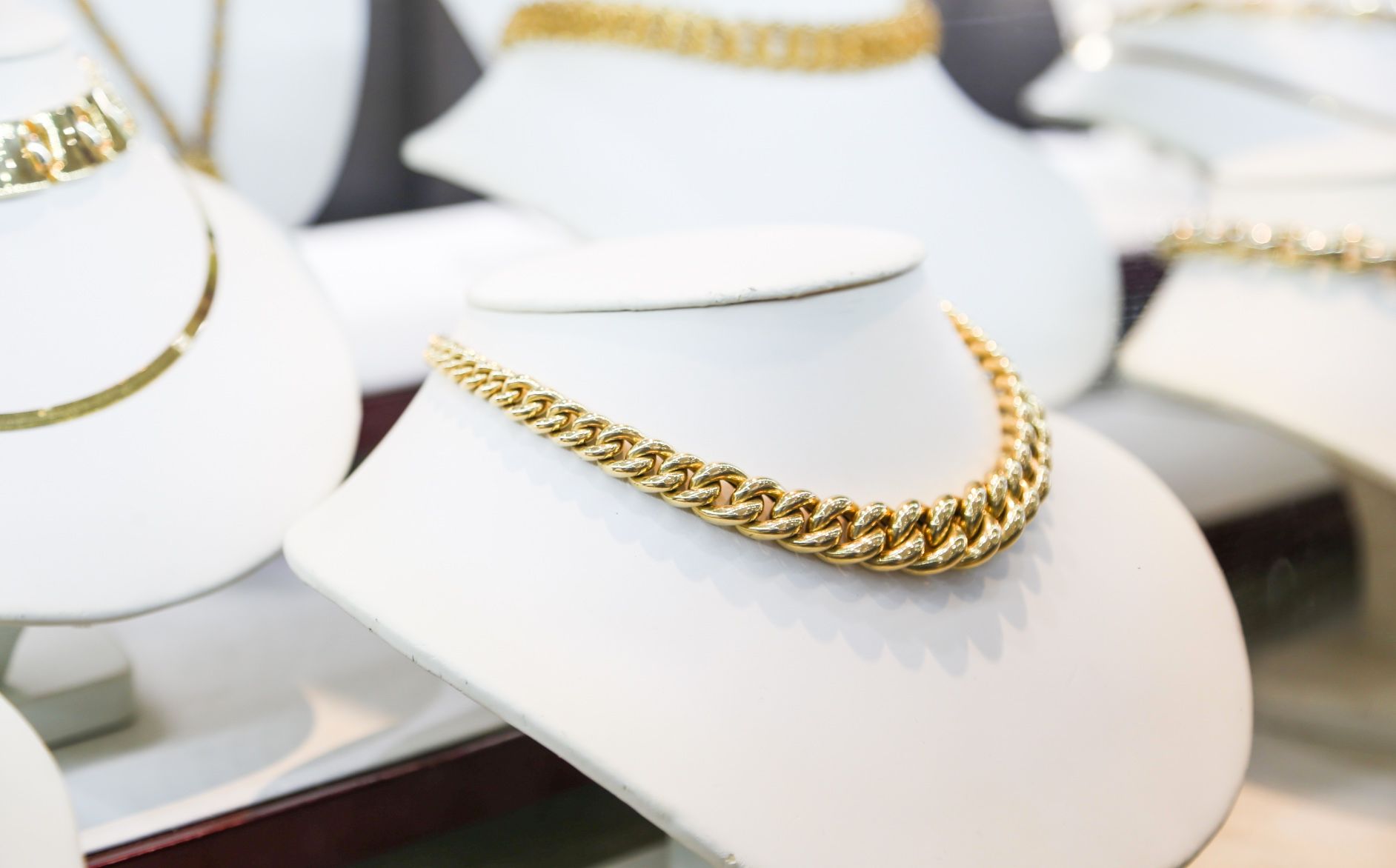 Display of elegant gold necklaces on white jewelry busts inside a retail store.