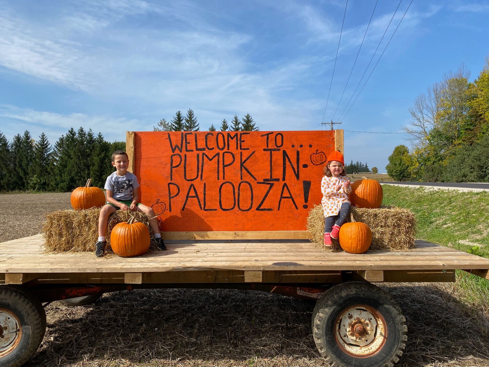 Two children are sitting on bales of hay next to a sign that says welcome to pumpkin palooza.