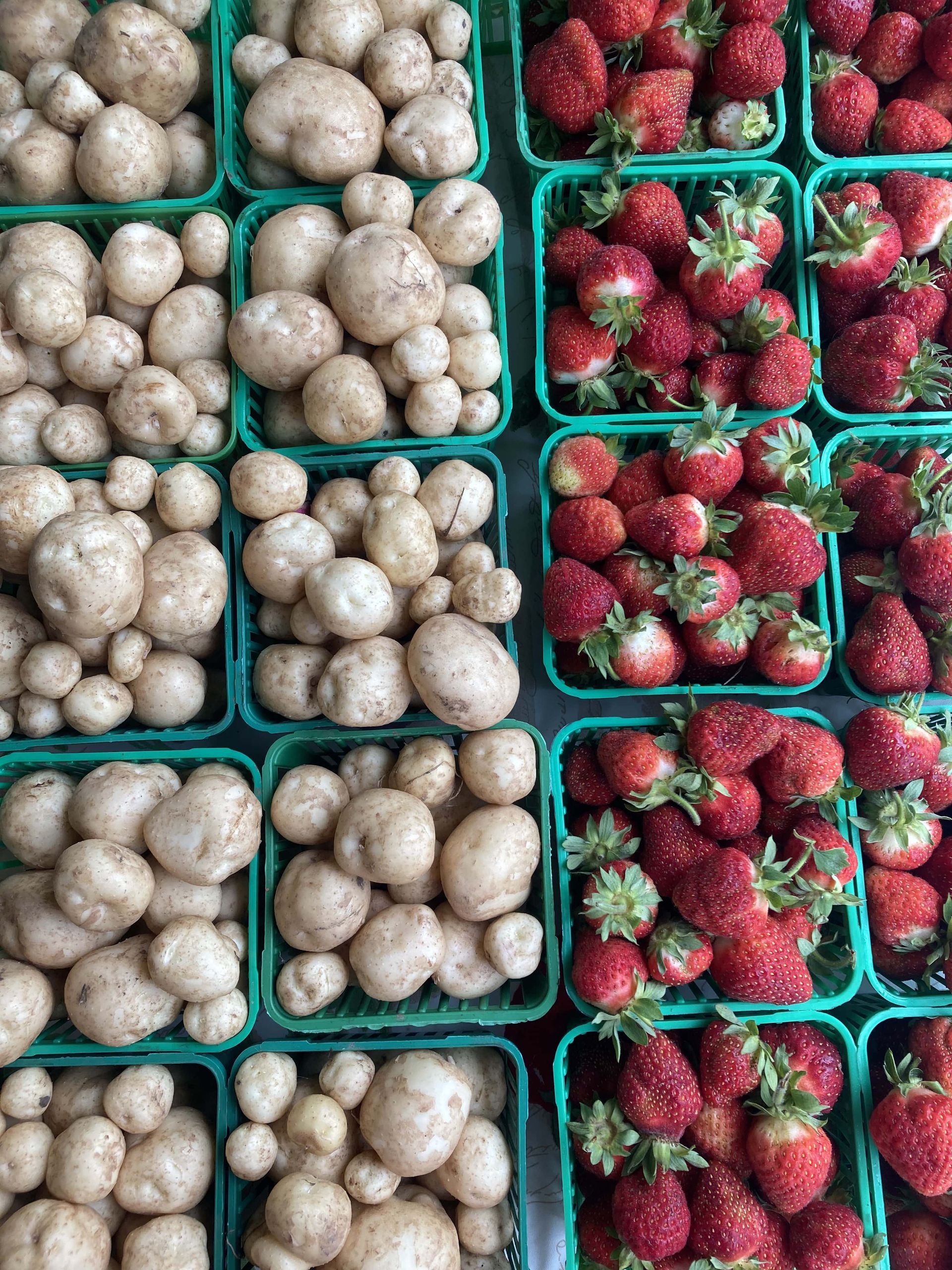 Strawberries and potatoes are in green baskets on a table.