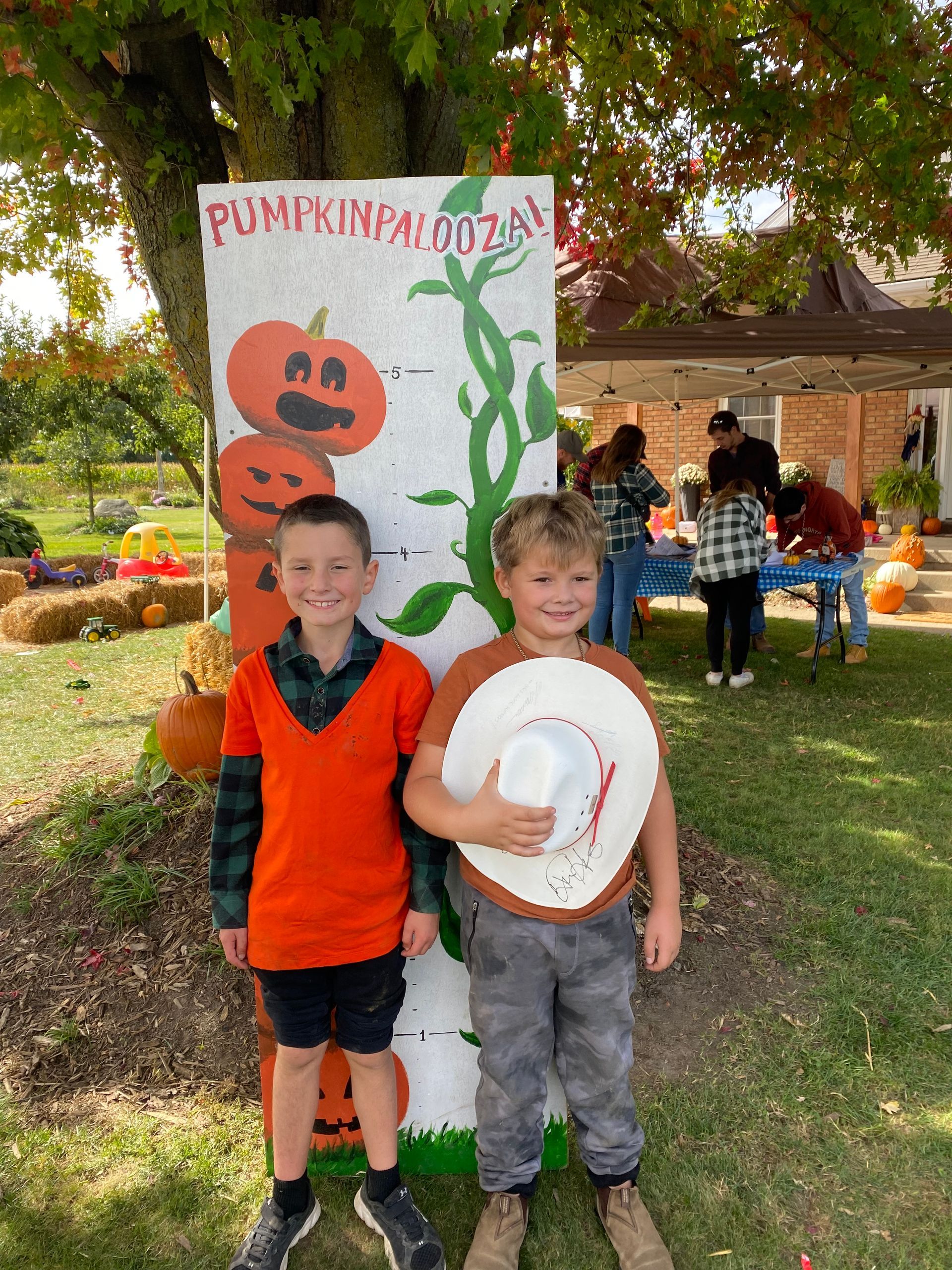 Two young boys are standing next to each other in front of a pumpkin patch sign.