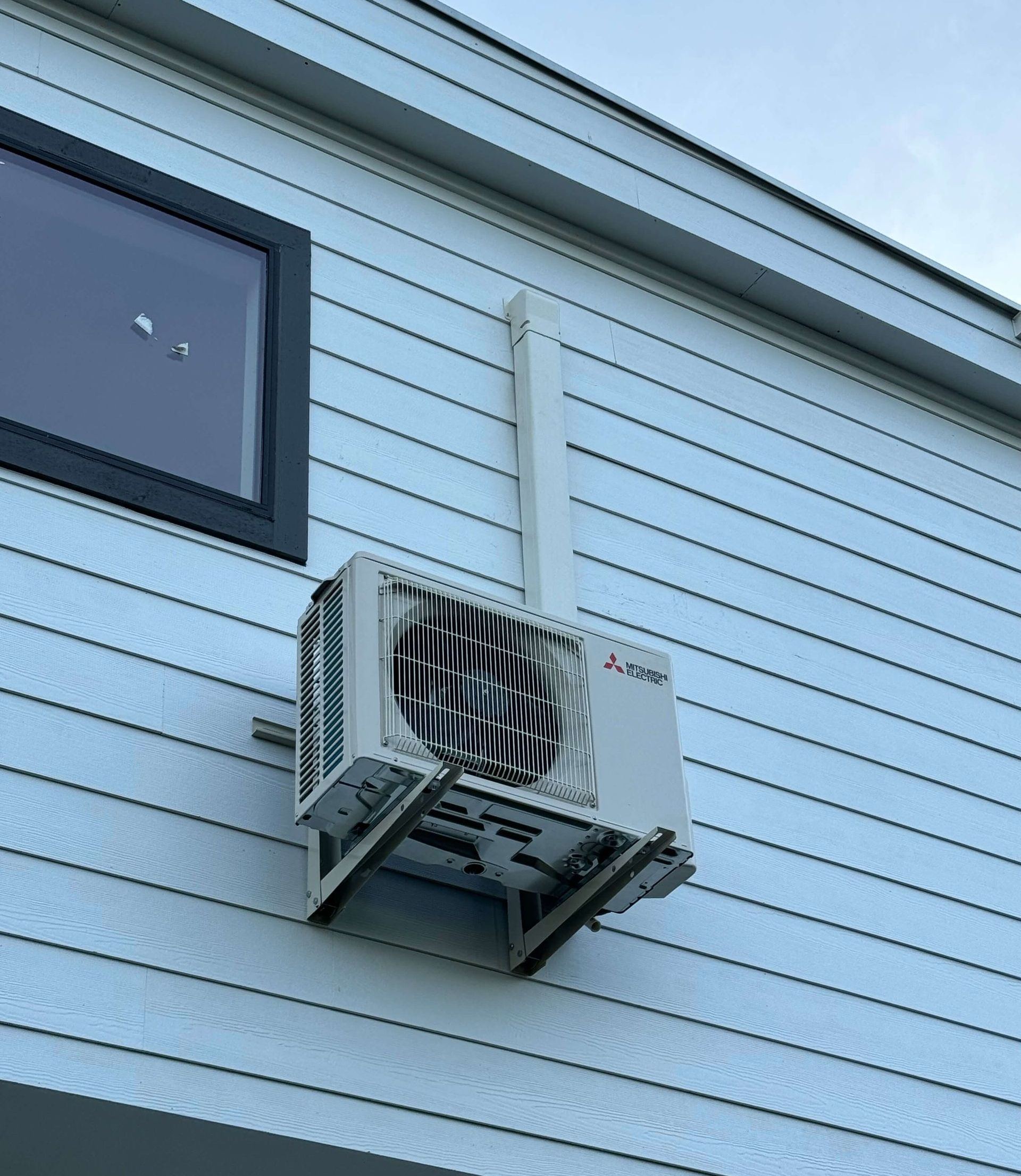 A white air conditioner is mounted on the side of a building.