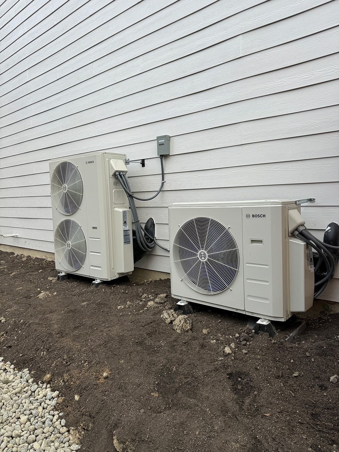 Two air conditioners are sitting next to each other on the side of a house installed by Ready Energy Solutions.