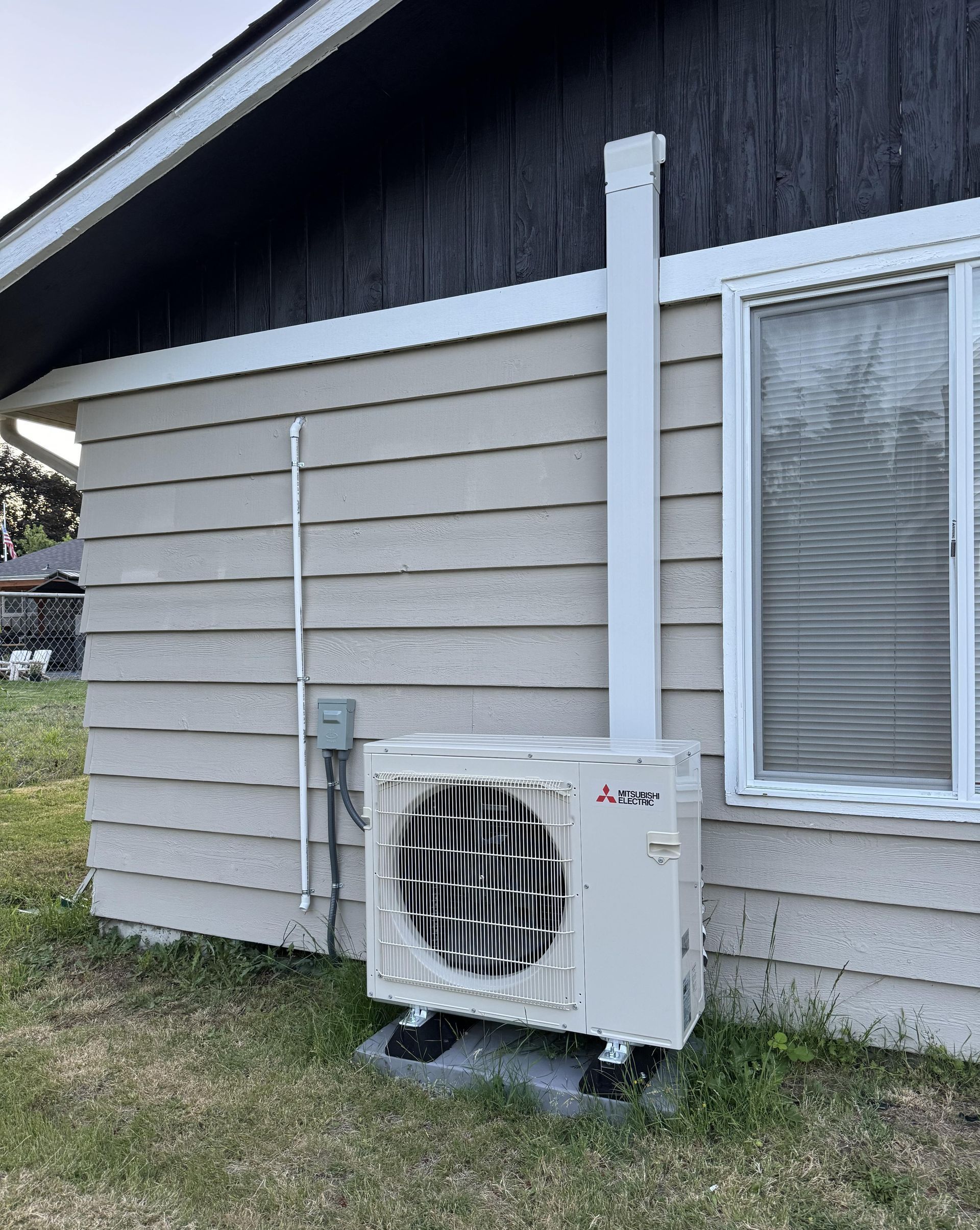 A white air conditioner is sitting on the side of a house next to a window.