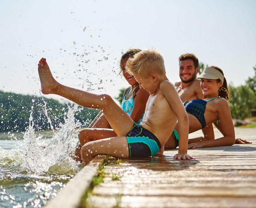 A family is sitting on a dock near a lake splashing water.