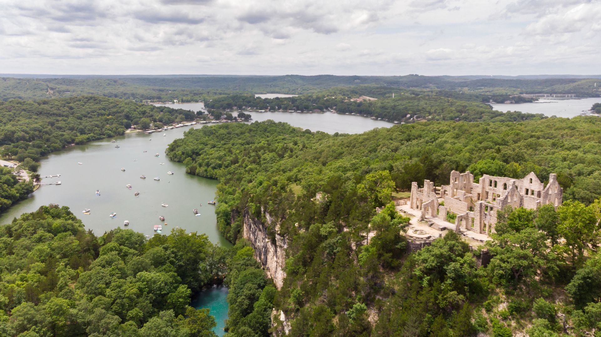 An aerial view of a castle on top of a cliff overlooking a lake surrounded by trees.