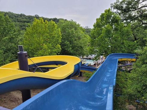 A blue and yellow water slide at a water park surrounded by trees.