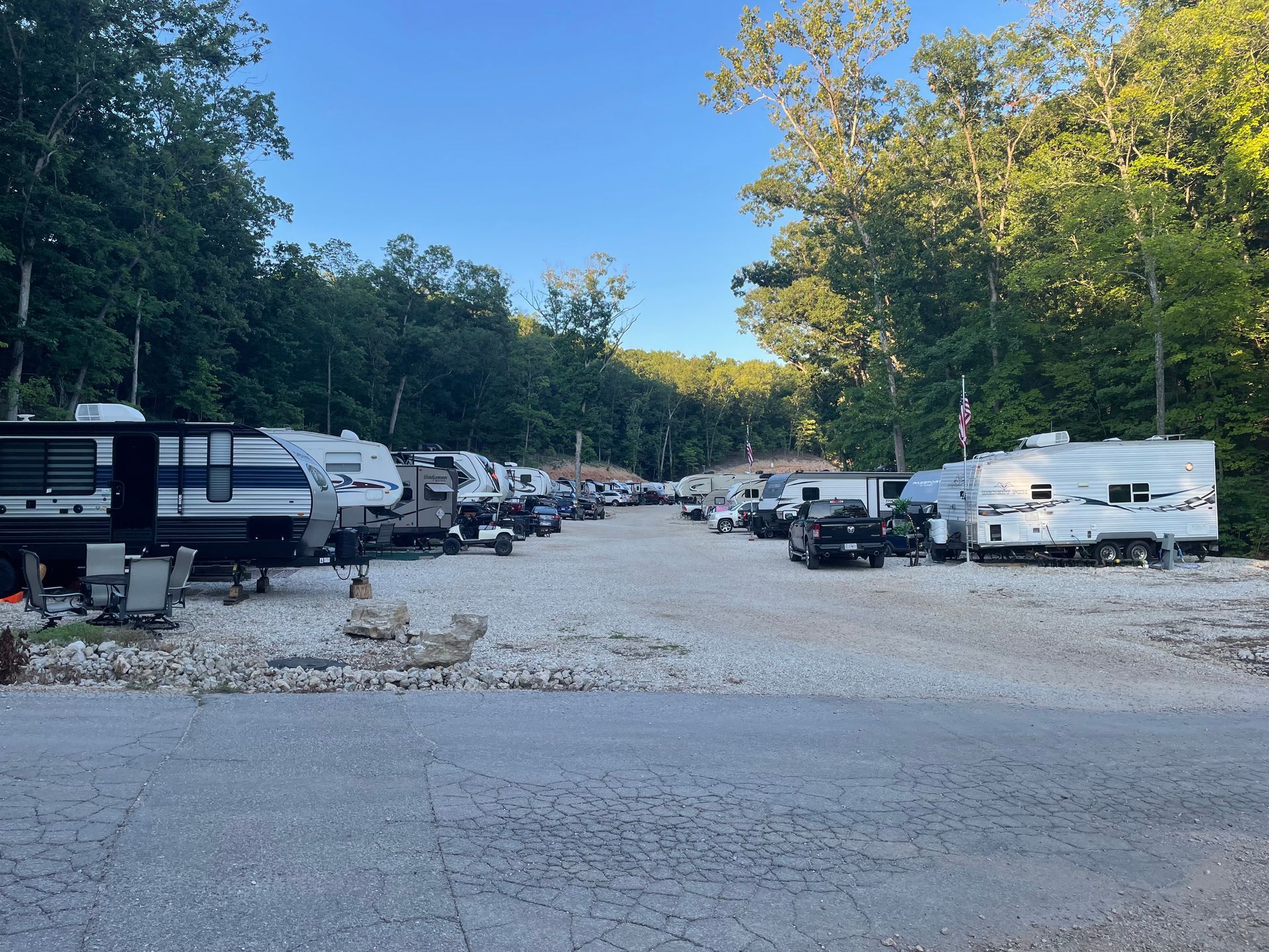 A row of rvs are parked in a parking lot surrounded by trees.