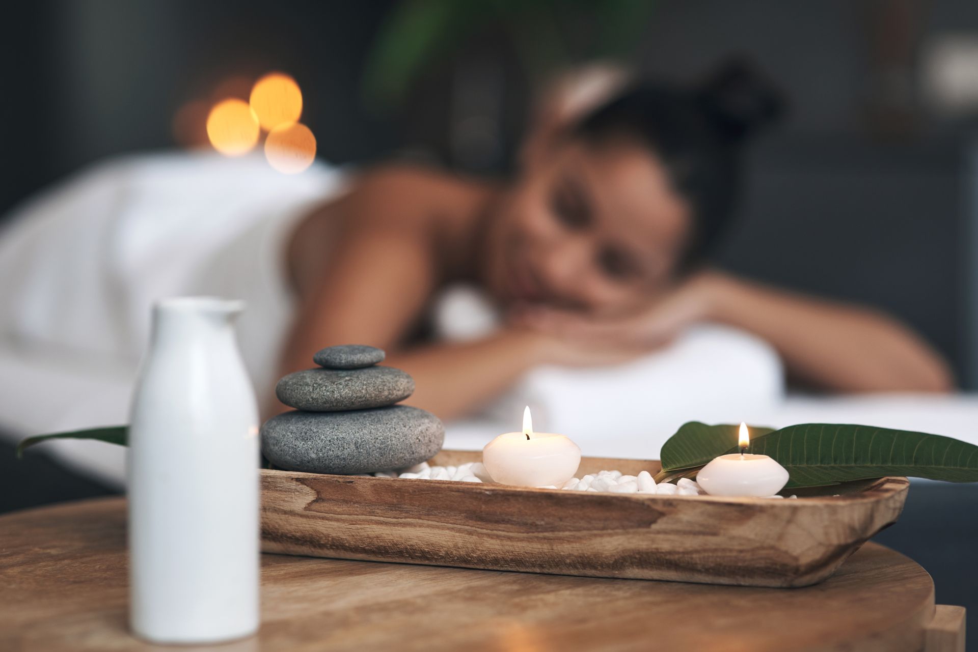 Spa scene: woman relaxing on massage table, candles and stones in foreground.