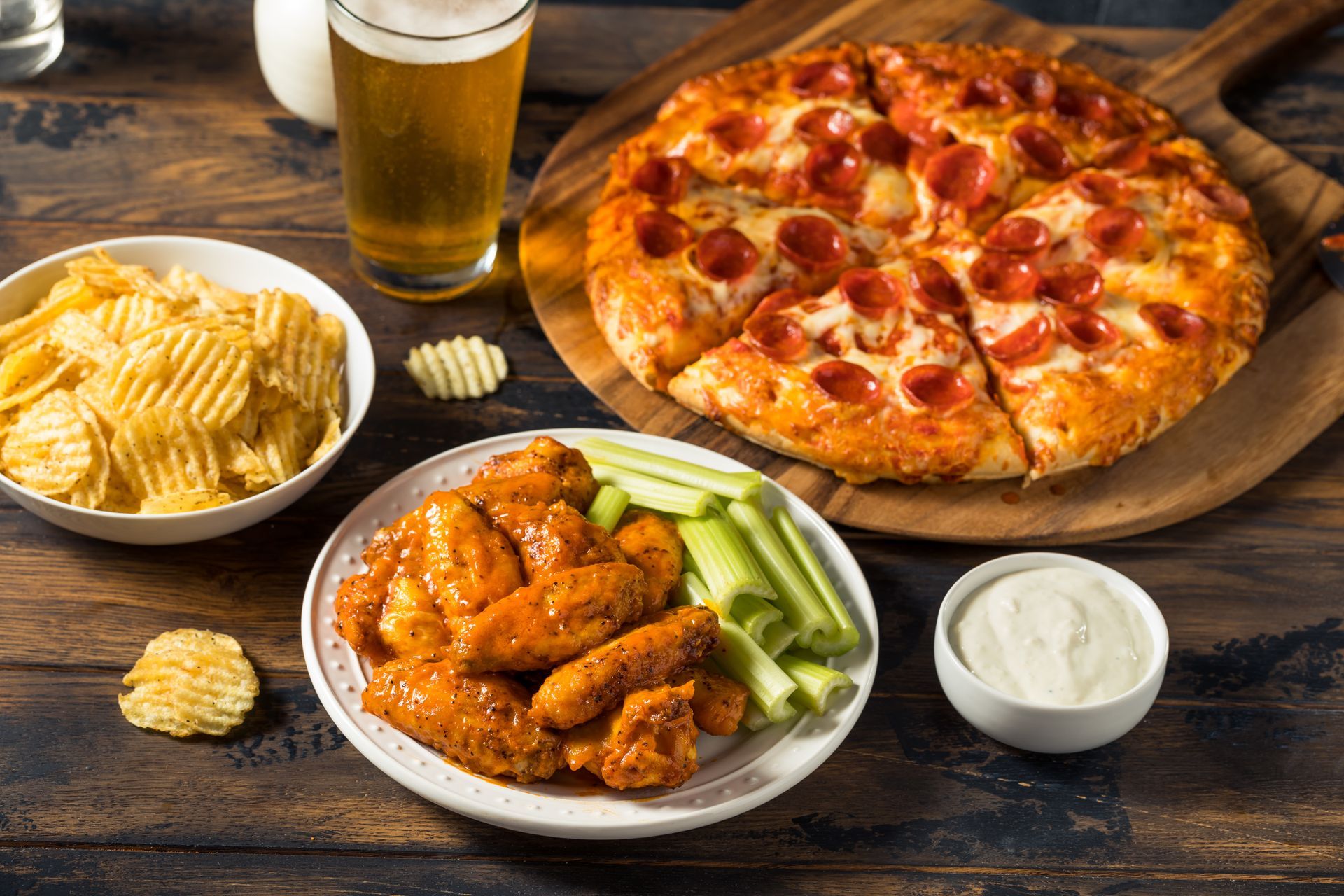 Pizza, chicken wings, chips, and beer on a wooden table.