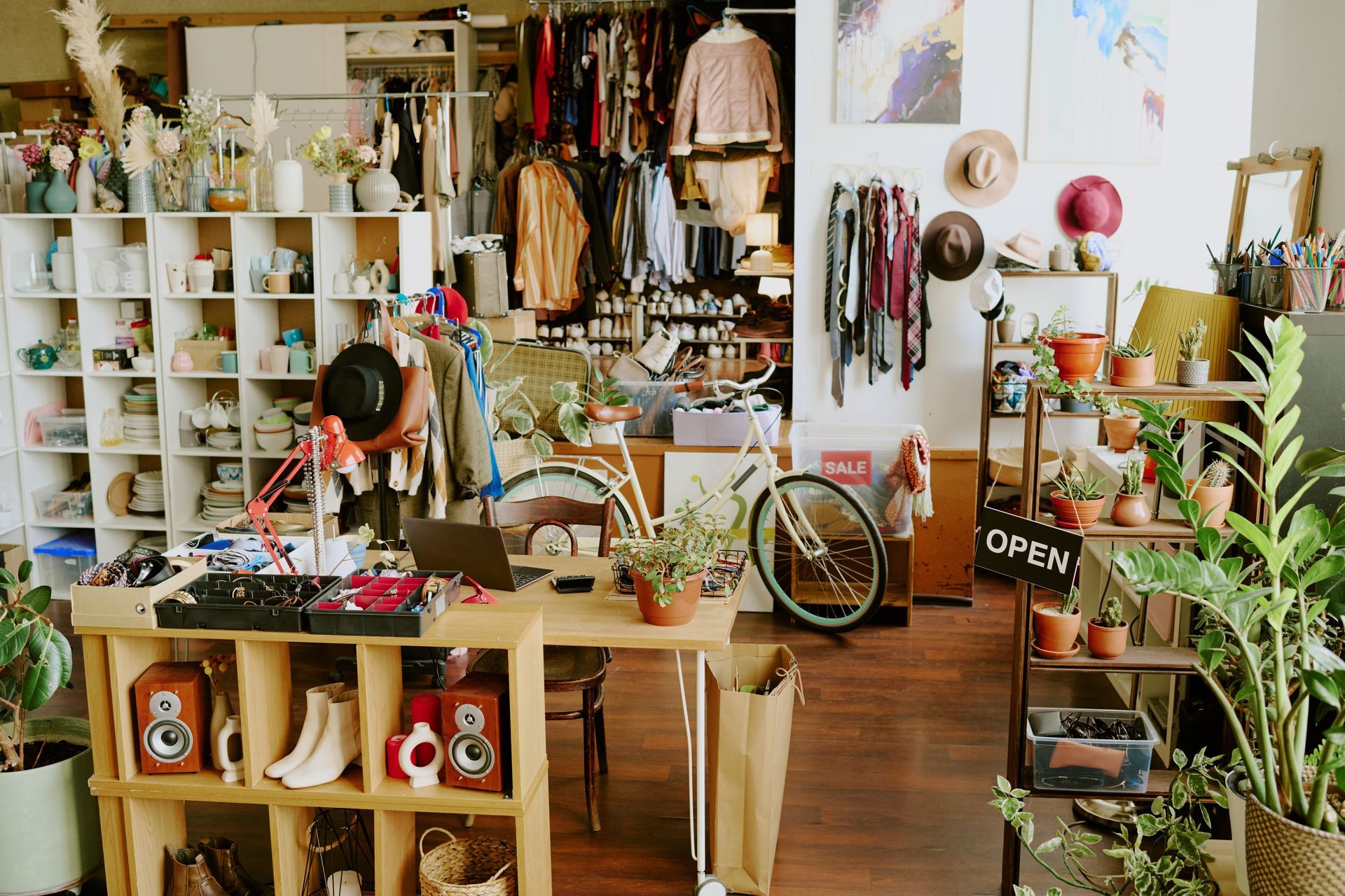 Vintage clothing and goods shop interior with racks, shelves, plants, and a bike wheel.