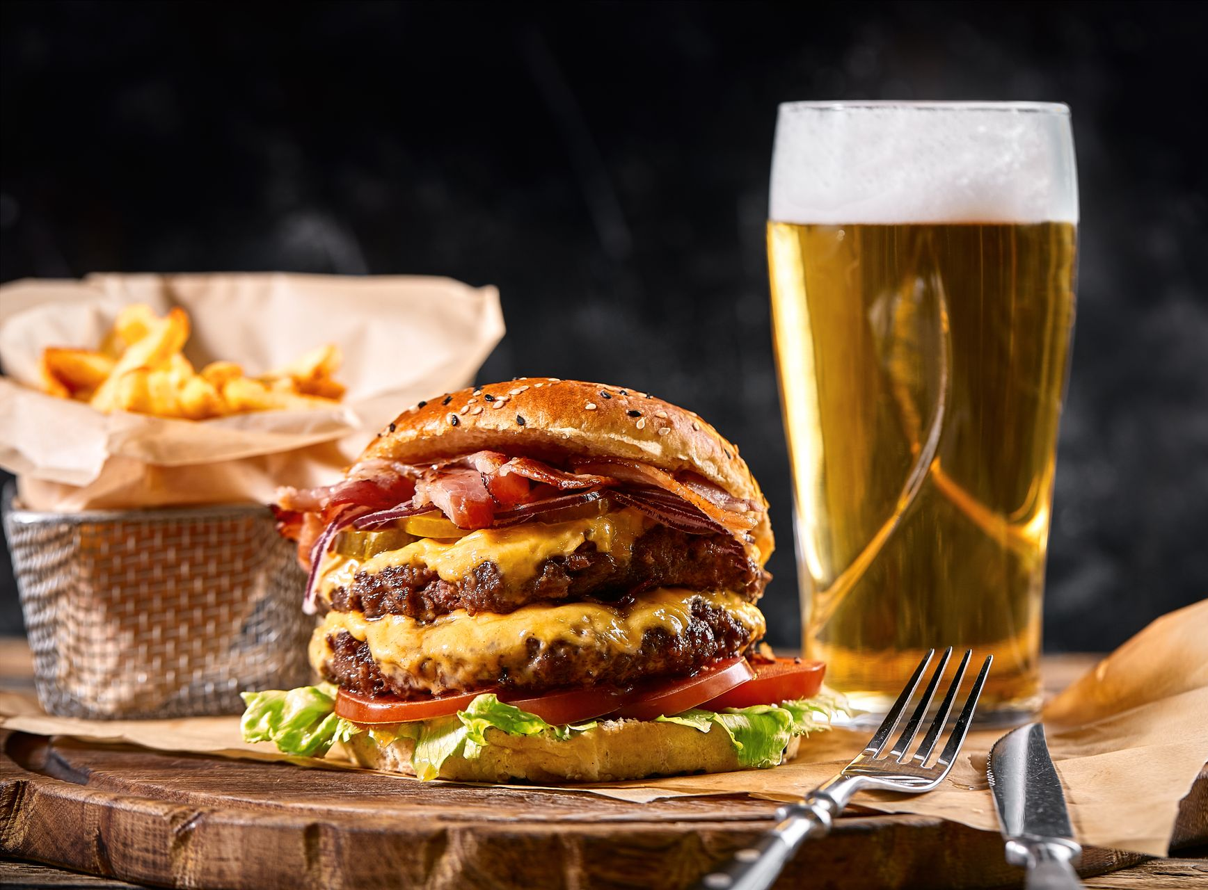 Double cheeseburger with bacon, fries, and beer on a wooden board.