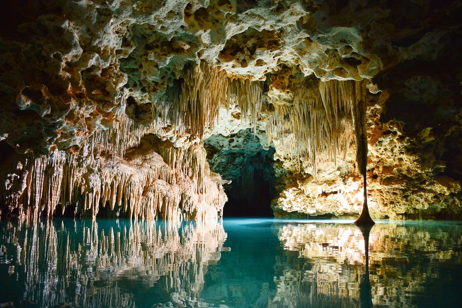 Cave interior with stalactites and turquoise water reflecting the rock formations.