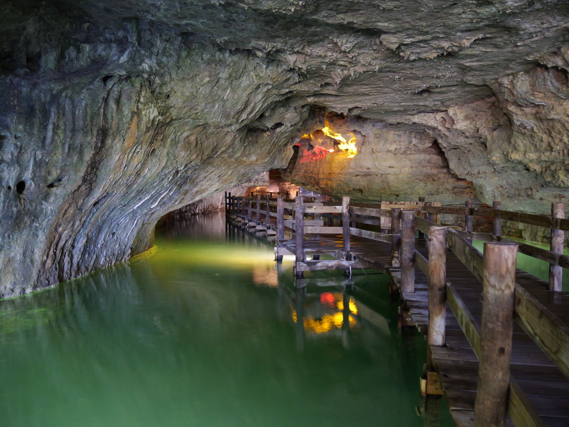 Cave with green water, wooden walkway, and illuminated interior.