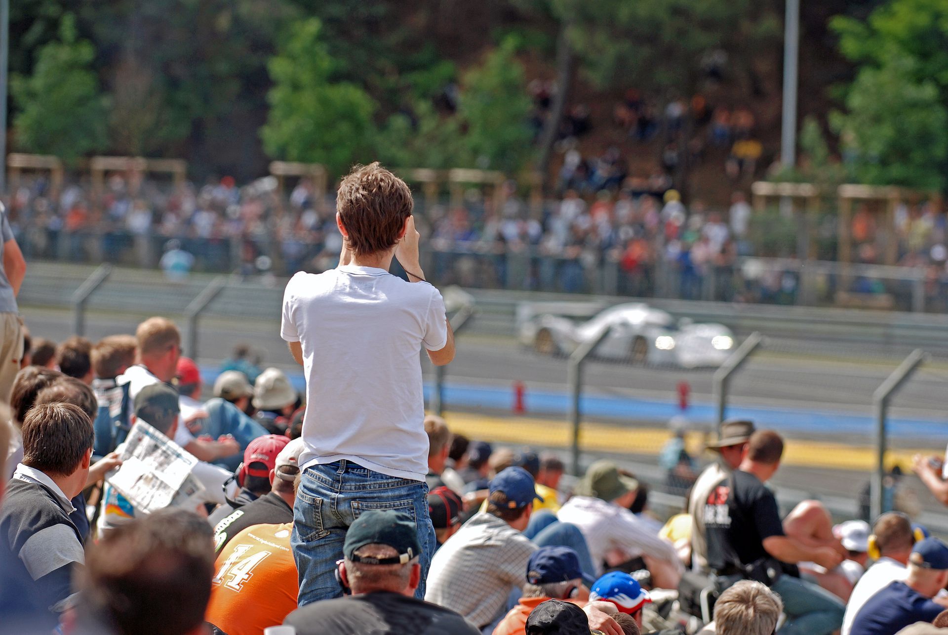 Spectators in a grandstand watching a blurry race car speed by on a track.
