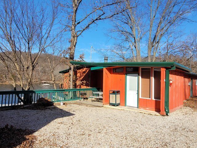 A small red house with a green roof is sitting next to a lake.