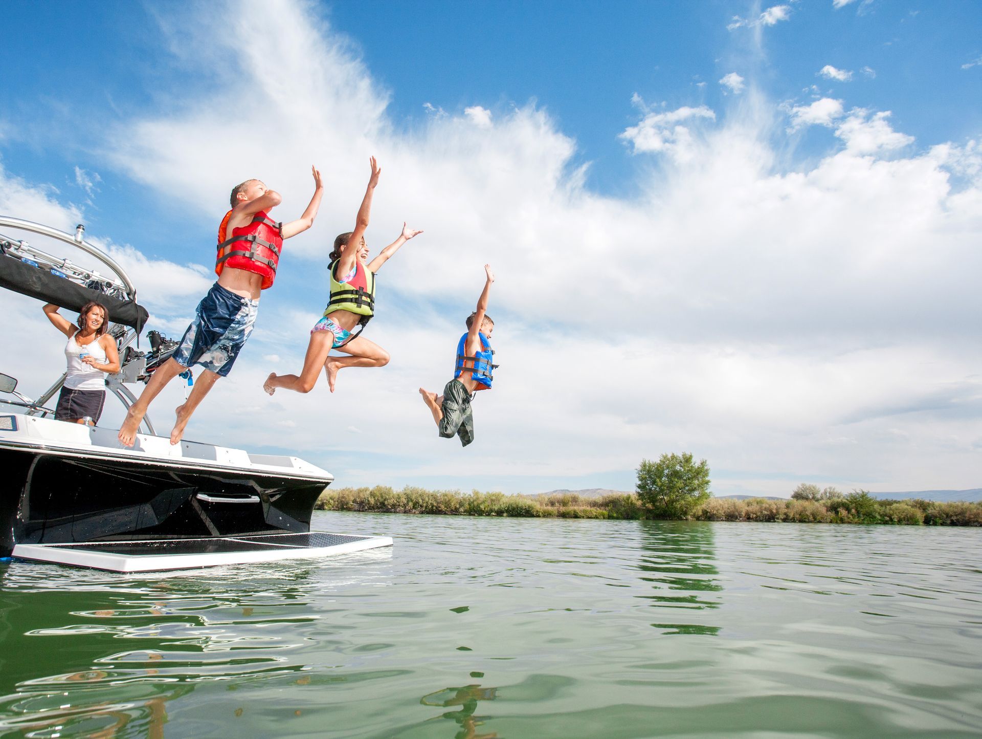 People jumping off a boat into water on a sunny day.
