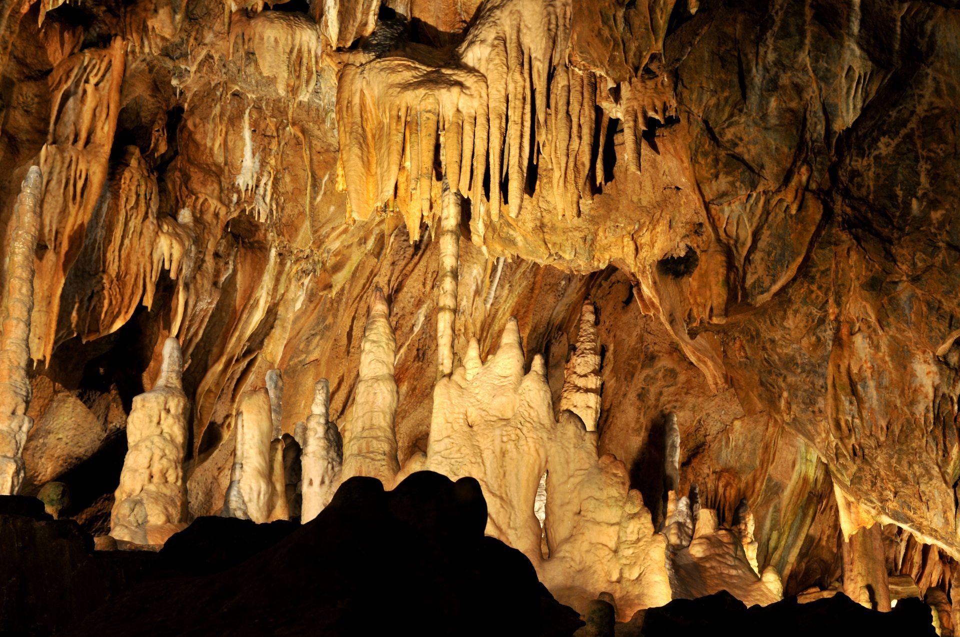 Cave interior with illuminated stalactites and stalagmites; orange and brown tones.