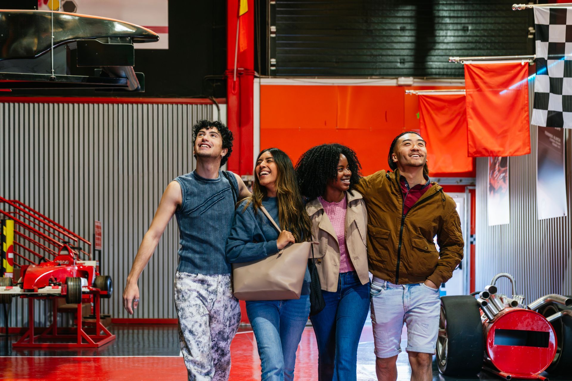 Four people look upward while walking through a racing-themed building with display cars and banners.