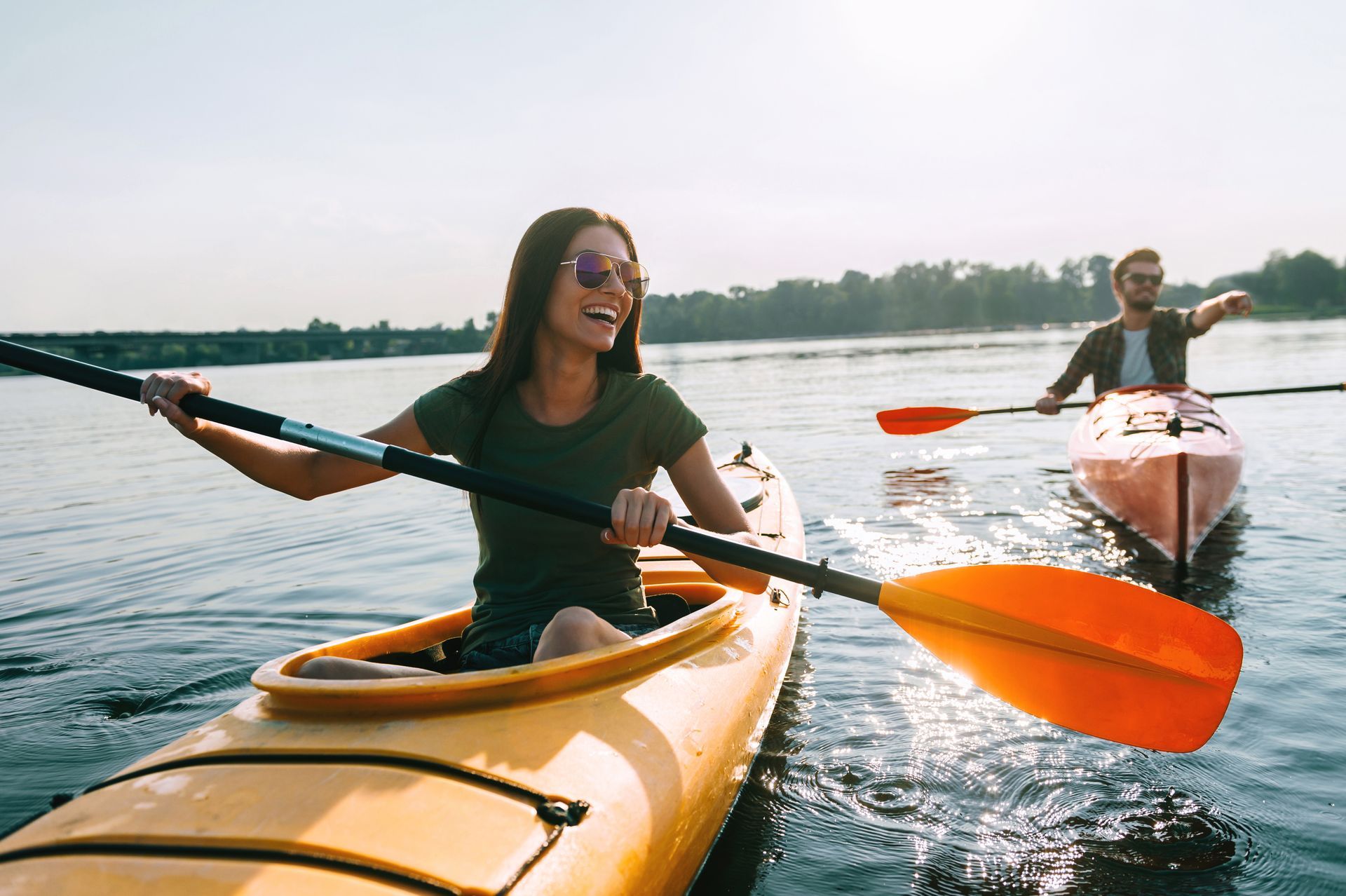 Woman kayaking on a sunny day, smiling, with a man in a kayak behind her.