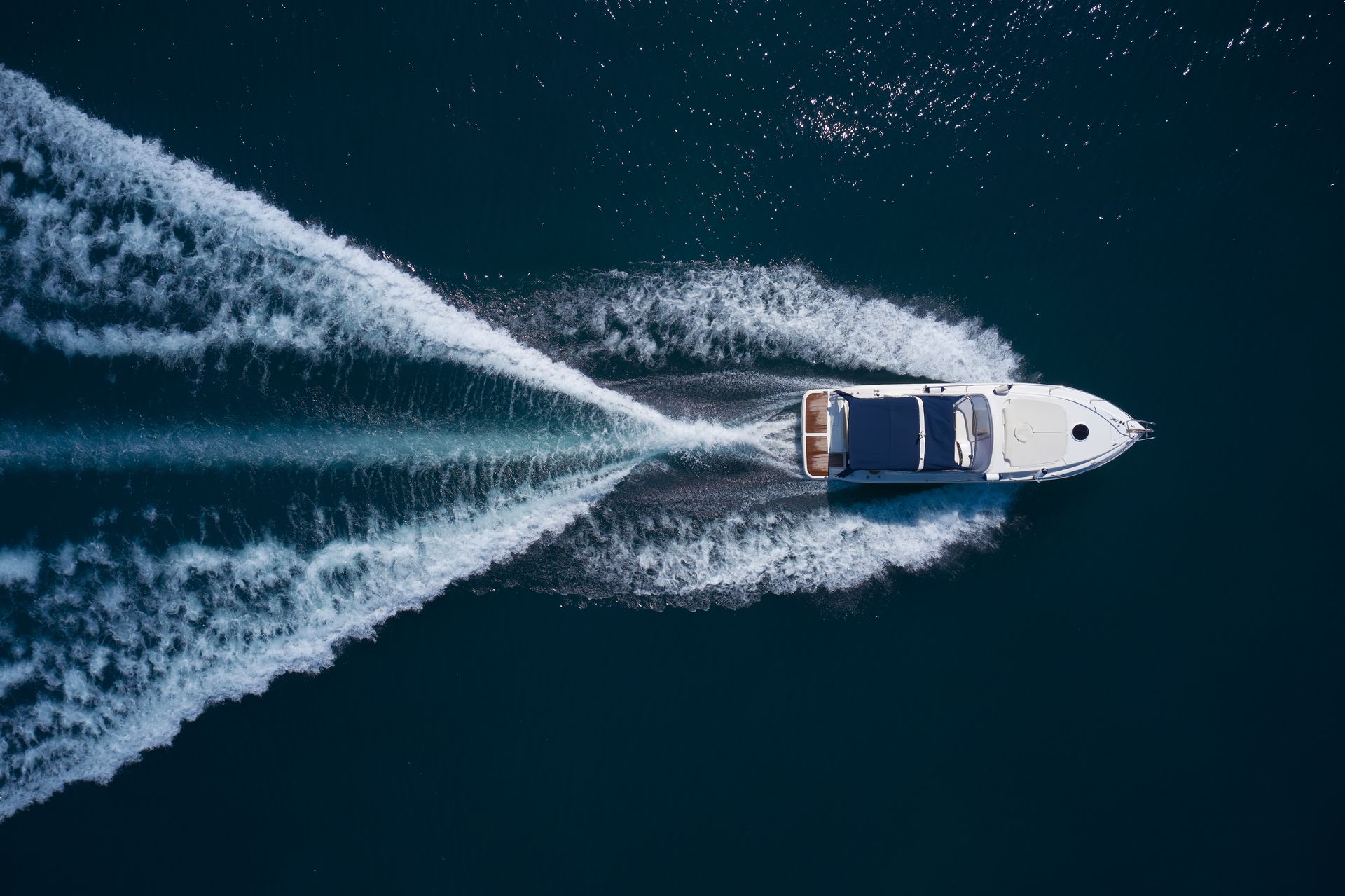 Boat speeding across dark blue water, creating white wake. Overhead view.