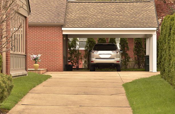 Driveway leading to a brick house garage with a car parked inside, bordered by green hedges.