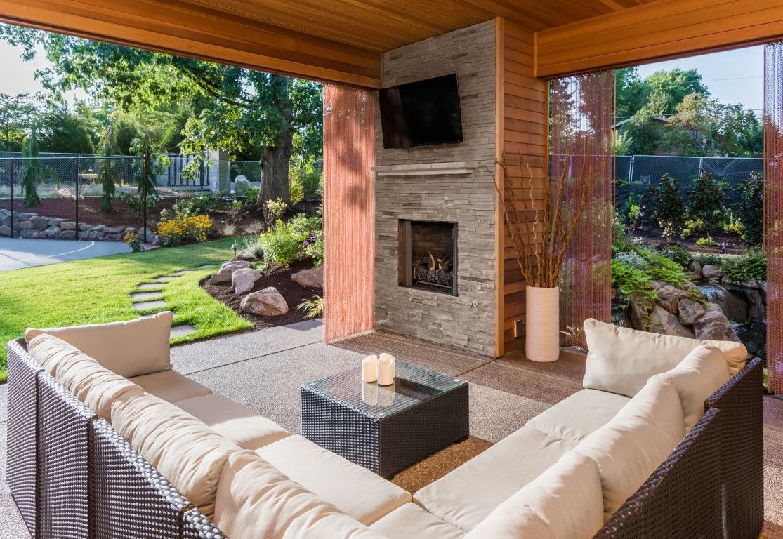 Covered patio with wicker seating, a fire pit, fireplace, and view of a landscaped yard