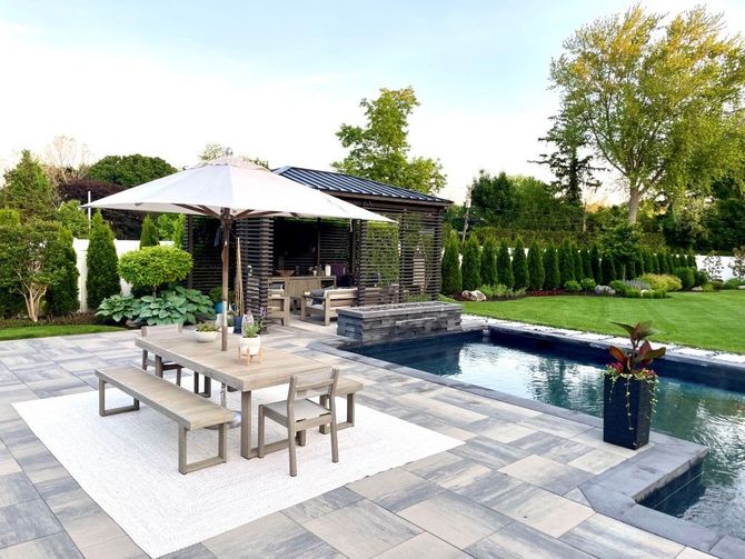 Backyard pool patio with dining table, umbrella, and lounge chairs beside a modern water feature