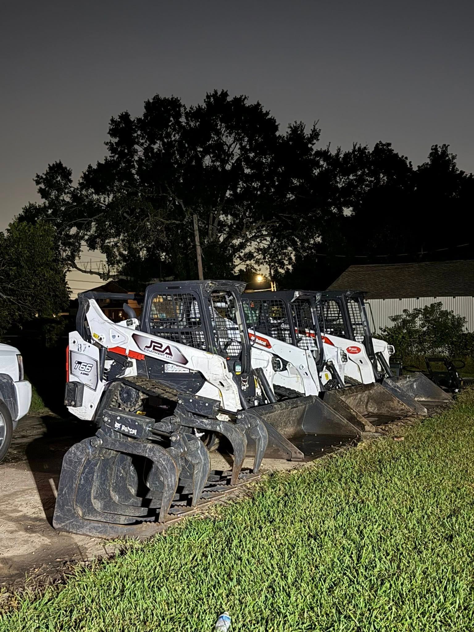 A row of white Bobcat skid-steer loaders with large buckets parked in a grassy field at twilight.
