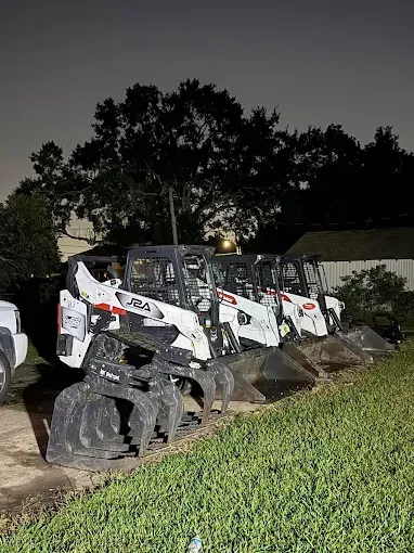 A line of white Bobcat skid-steer loaders parked in a grassy area at night.