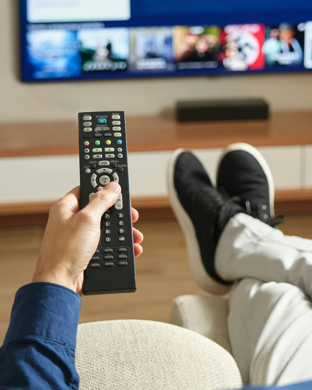 En mand sidder i sofaen og ser tv og holder en fjernbetjening foran sig 