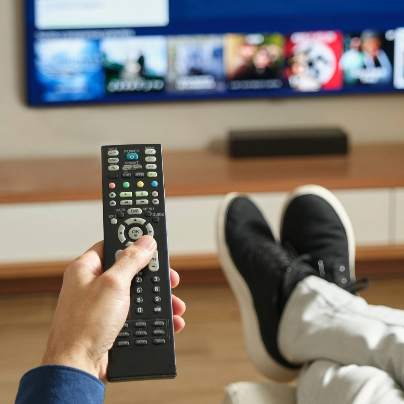 En person sidder i en sofa og holder en fjernbetjening foran et fjernsyn.