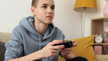 En ung dreng sidder på en sofa og spiller et videospil.