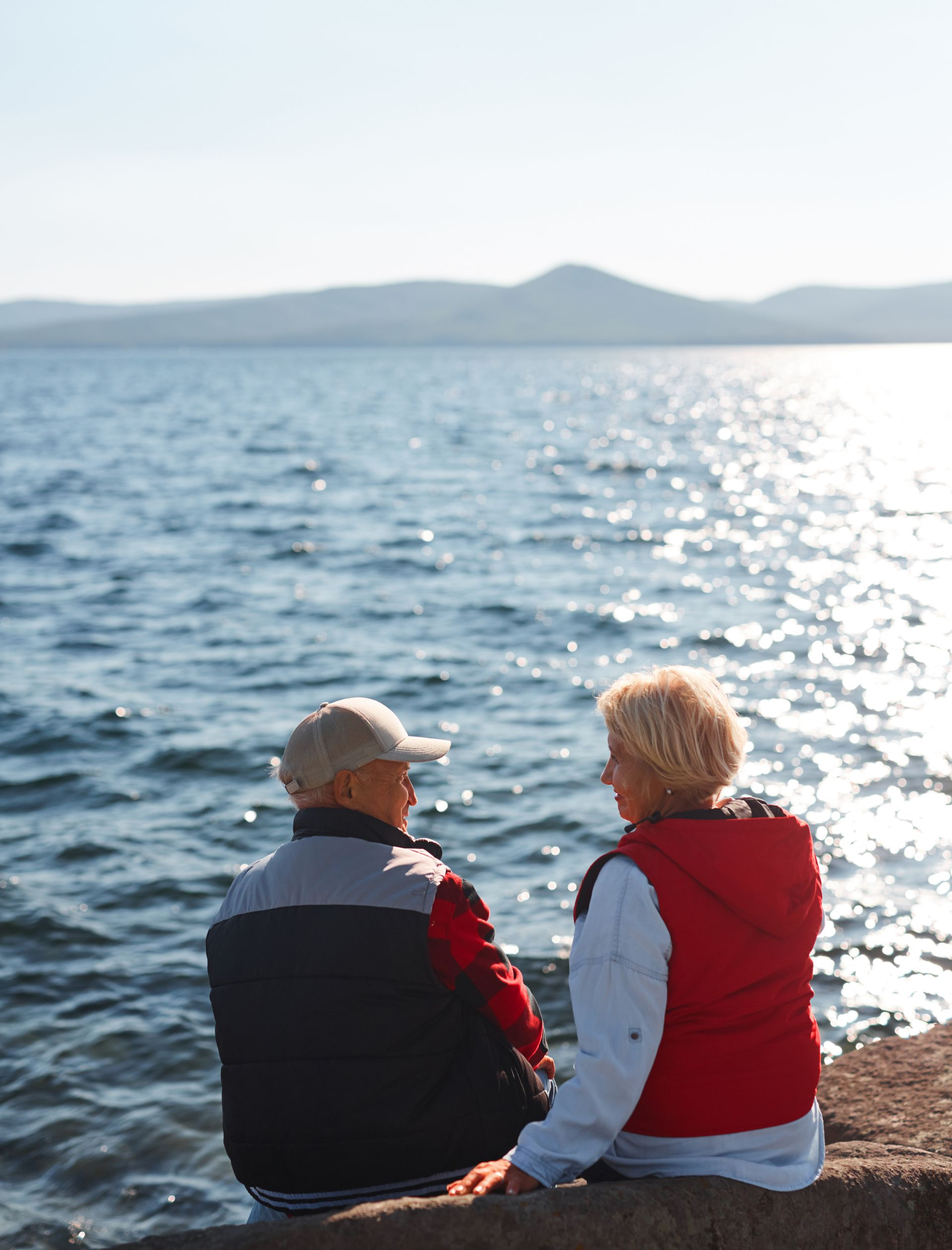 A woman is carrying a little girl on her shoulders in a field at sunset.