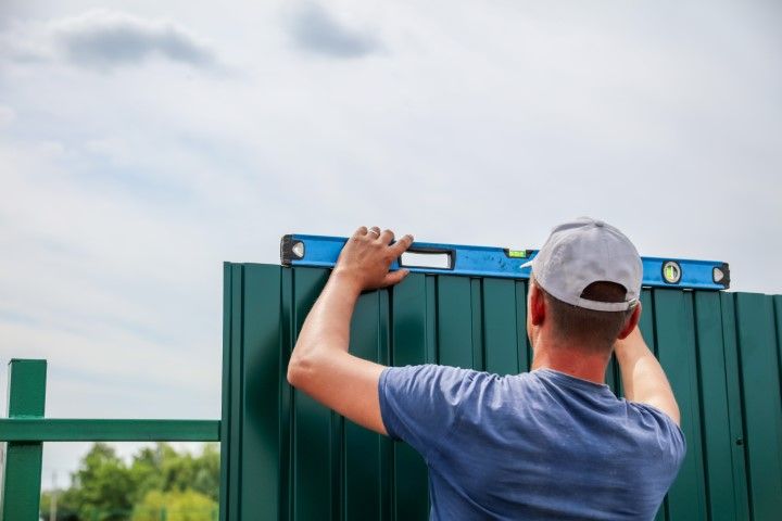 Installation professional for Lake Oswego Fence Pros using a level to check the alignment of a metal fence with the ground.