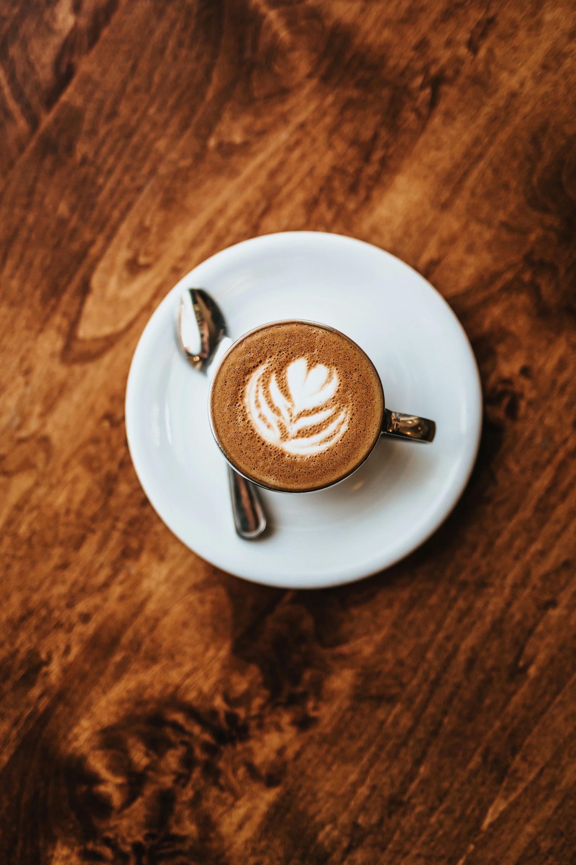 A cup of cappuccino on a saucer with a spoon on a wooden table.