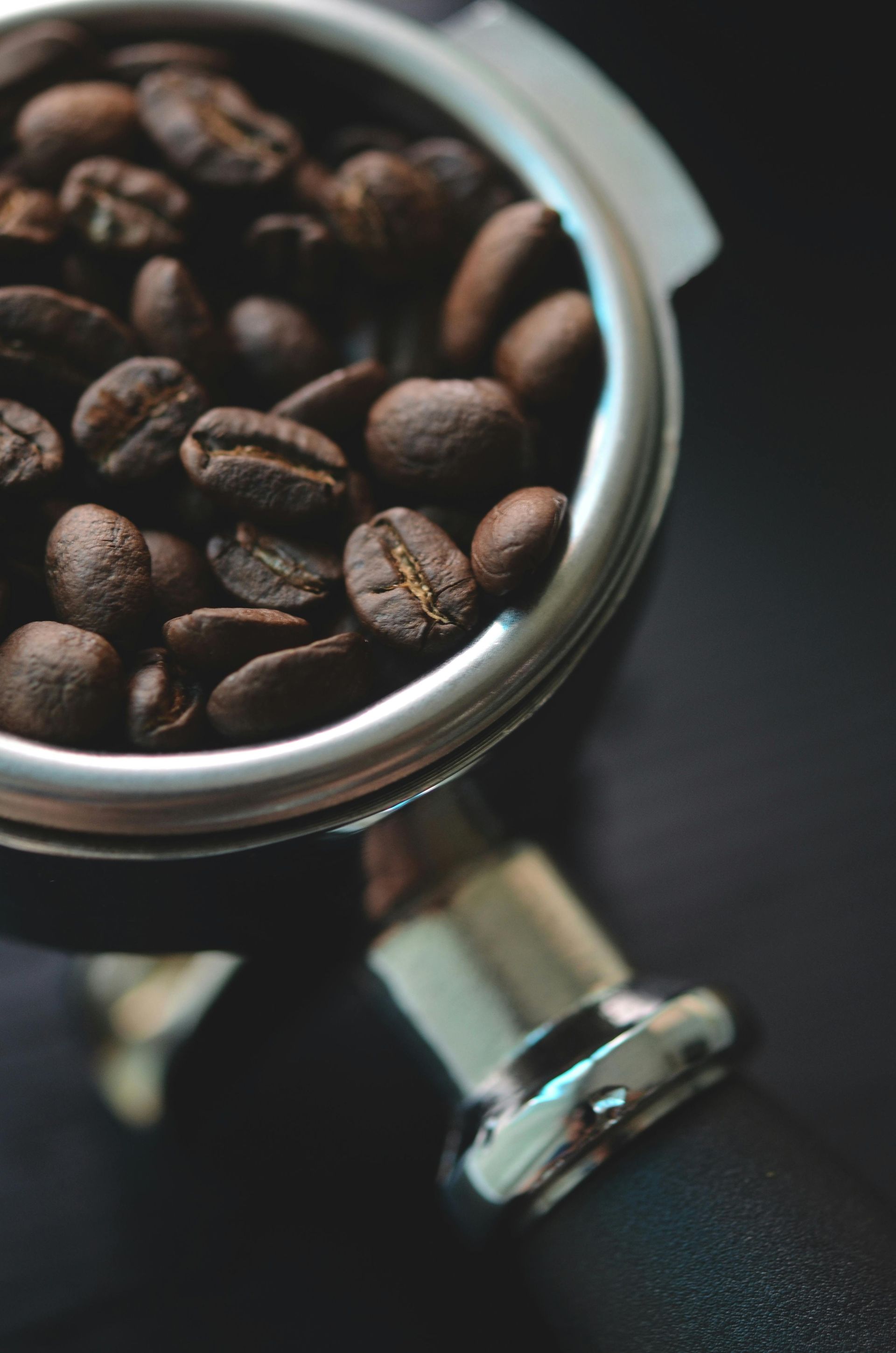 A metal container filled with coffee beans on a black surface.
