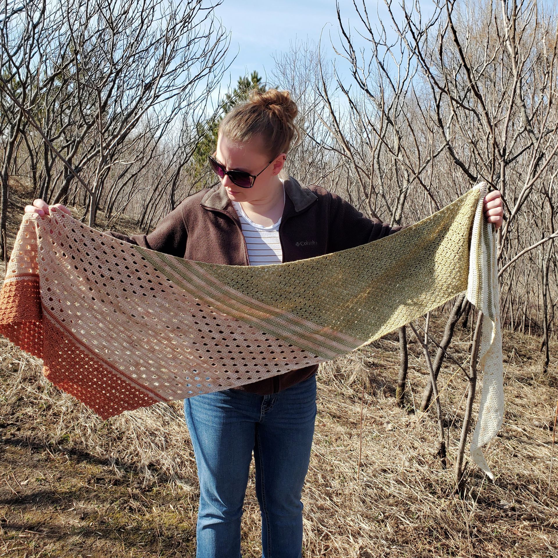 Woman wearing sunglasses, displaying a multi-colored shawl outdoors.