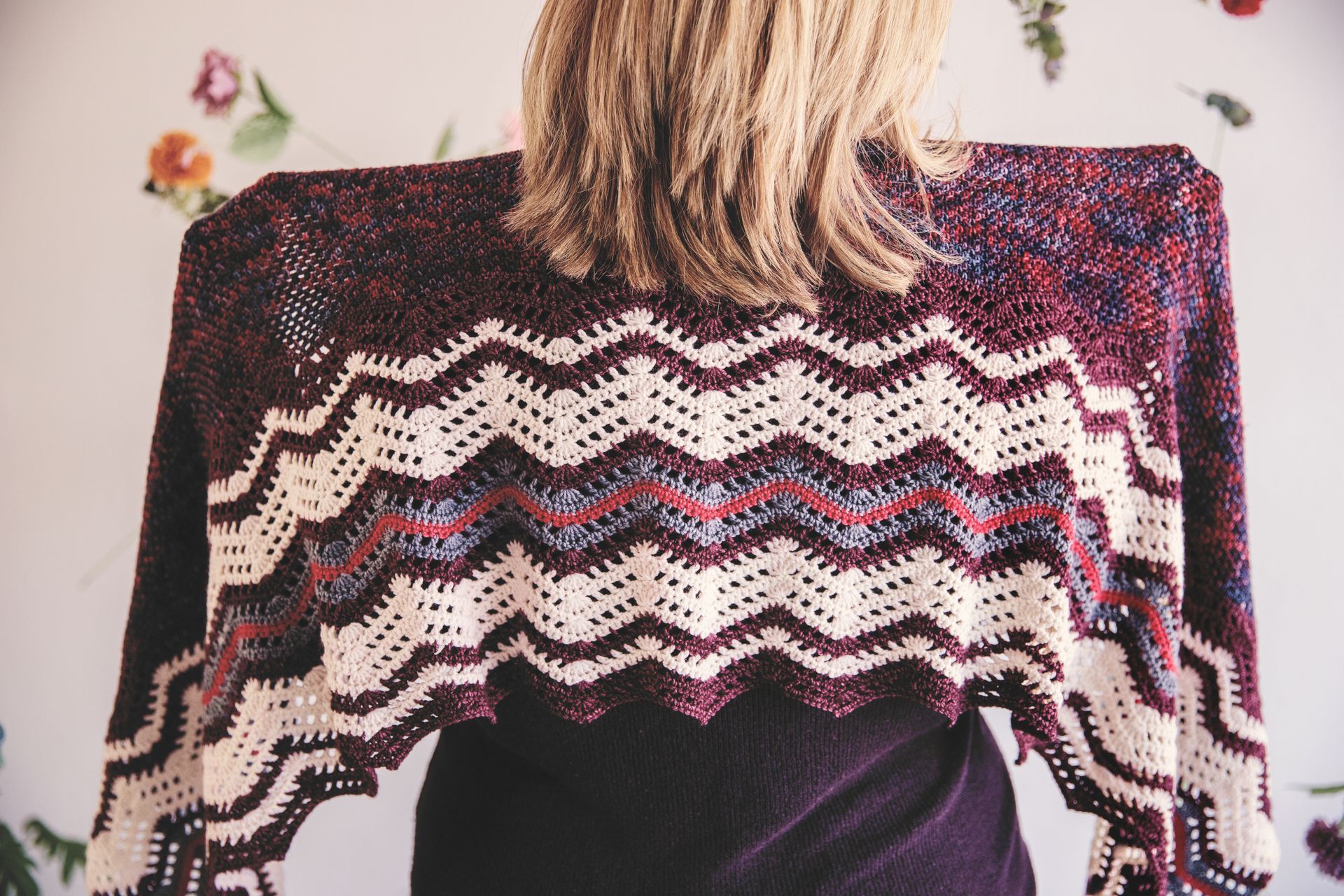 Woman wearing a crocheted shawl with a zigzag pattern in burgundy, cream, and blue colors.