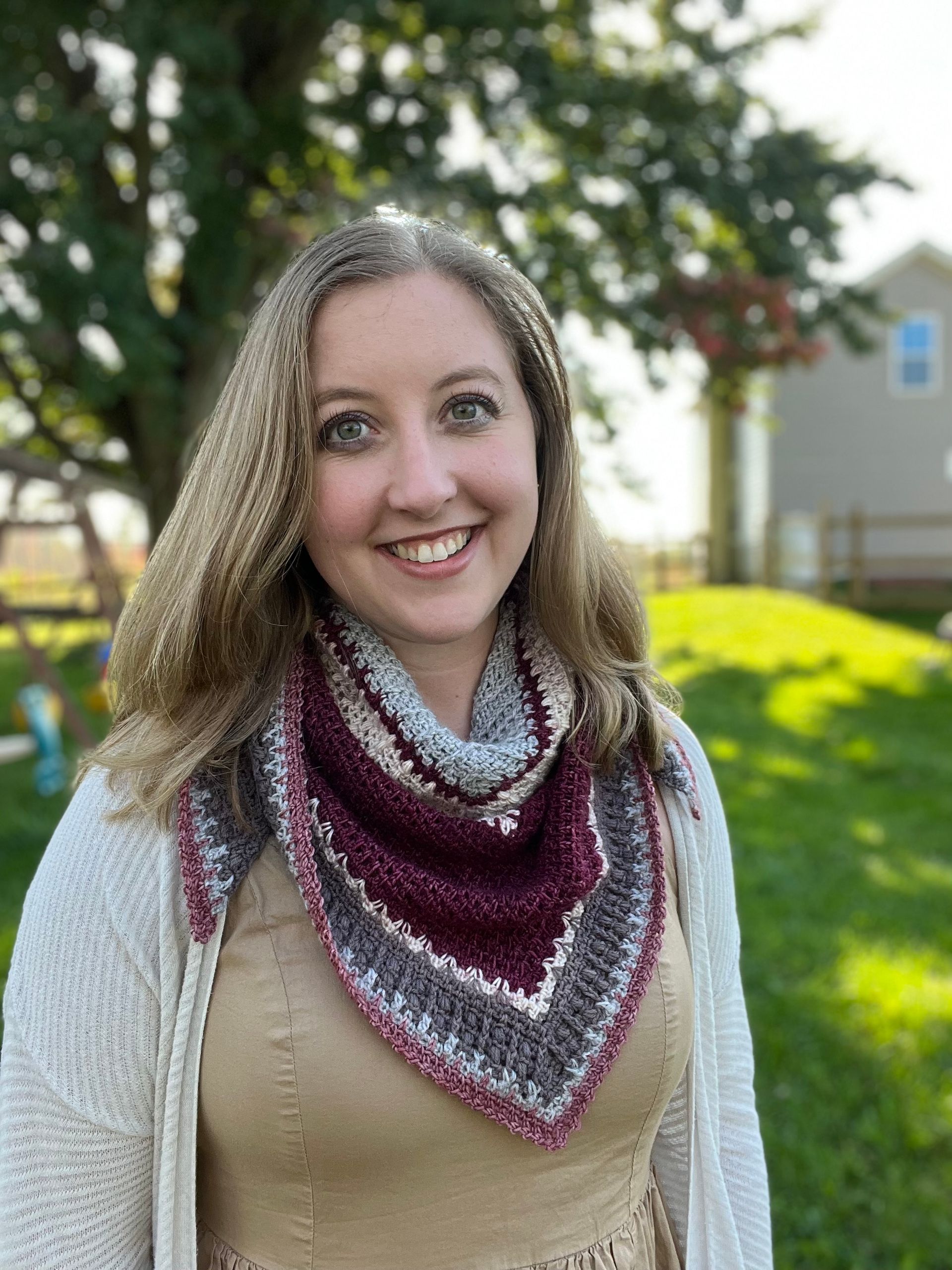 Woman wearing a maroon, gray, and white crocheted shawl smiles outdoors.