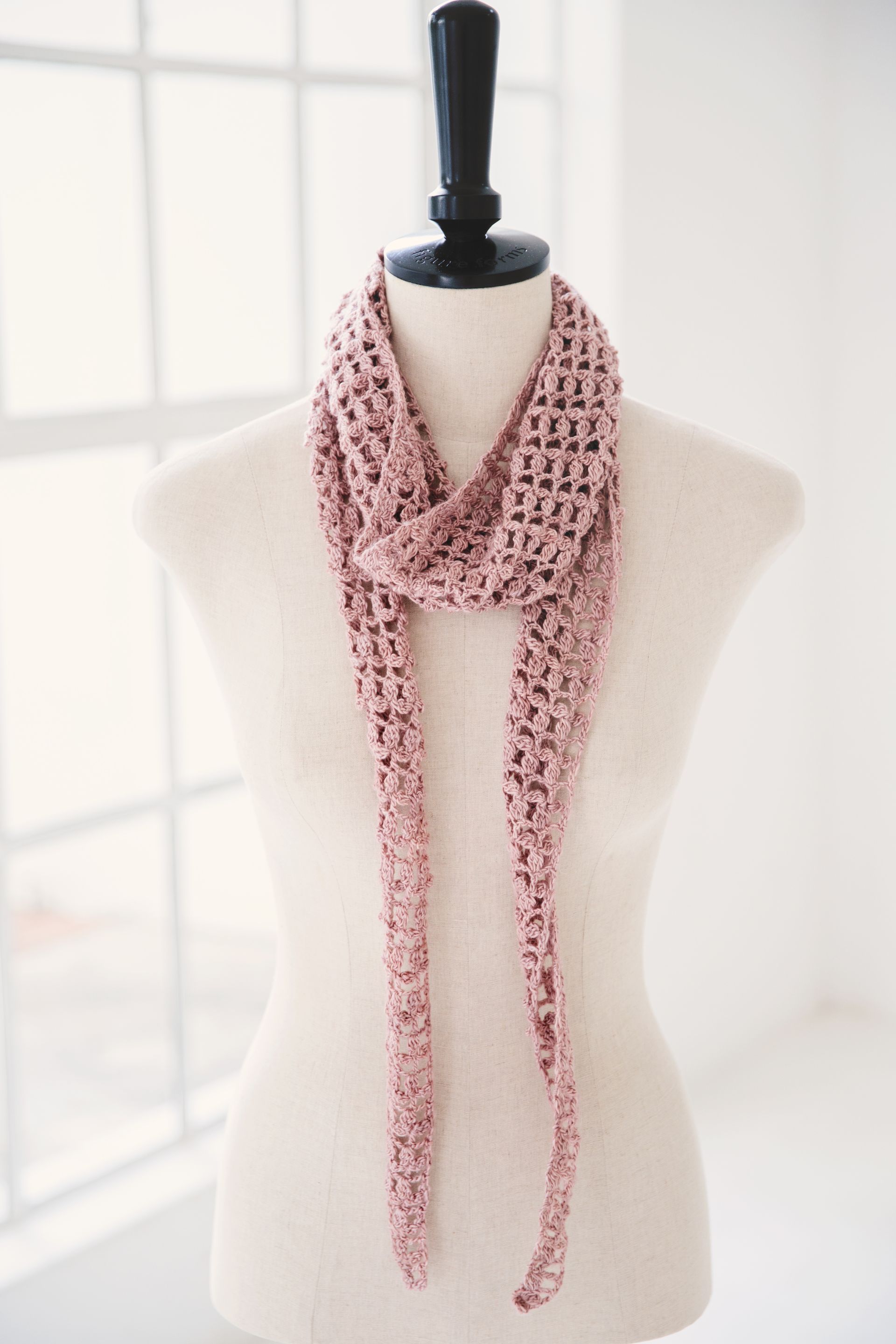 Pink crocheted scarf draped on a mannequin in front of a window.