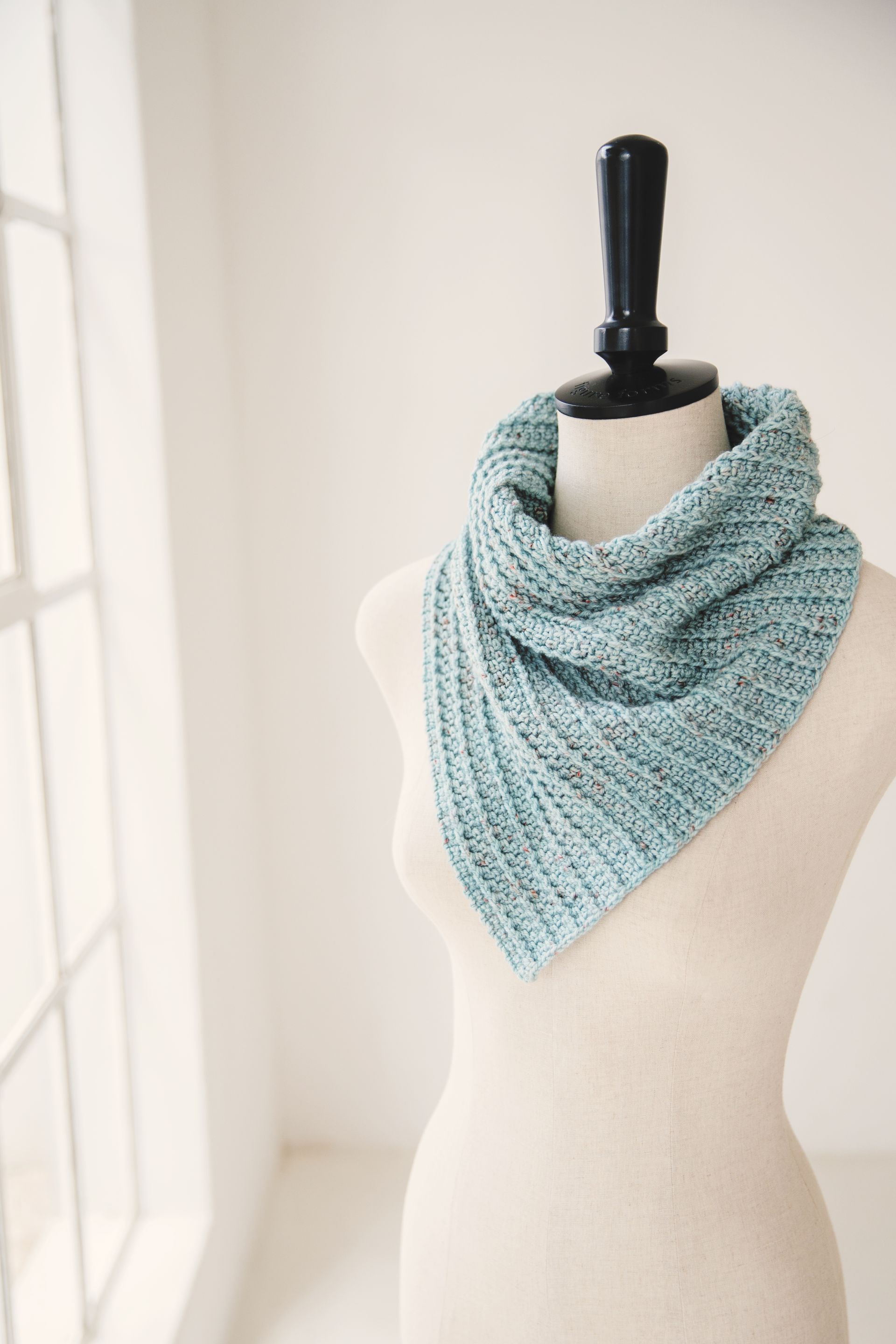 A teal knitted cowl on a mannequin in front of a window.